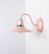 Aplique de parede com um design clássico e cores contemporâneas. O aplique é composto por uma base circular rosa clara, de onde se estende um braço curvo, que forma um arco gracioso e sustenta o chapéu do candeeiro, rosa claro também. O chapéu tem um formato cónico invertido, com uma borda ligeiramente levantada, que direciona a luz para baixo. O interior do chapéu é branco. No topo do chapéu, há um suporte circular em níquel polido, com três braços que fixa o chapéu ao braço curvo.