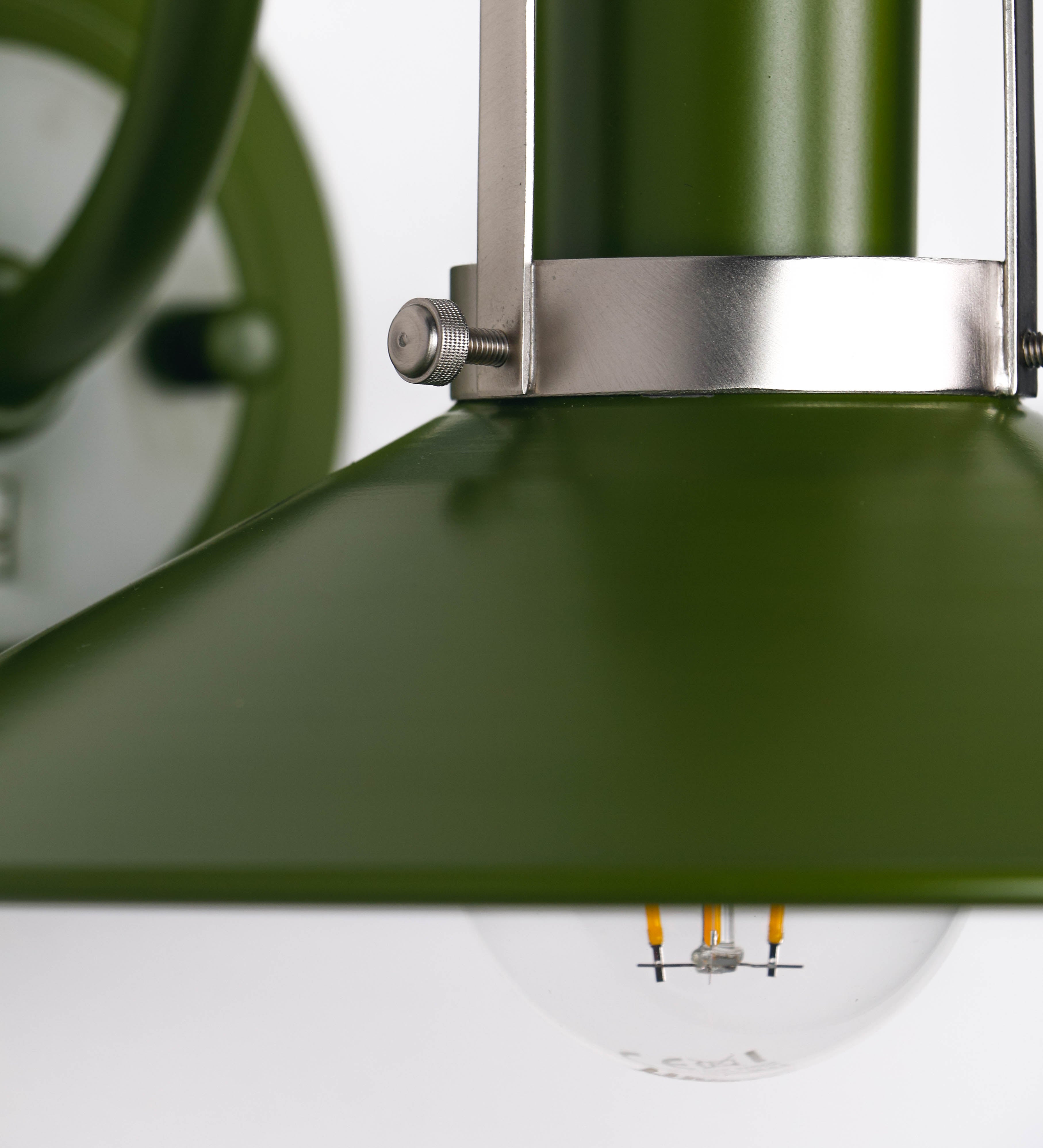 Aplique de parede com um design clássico e cores contemporâneas. O aplique é composto por uma base circular verde couve-de-bruxelas, de onde se estende um braço curvo, que forma um arco gracioso e sustenta o chapéu do candeeiro, verde também. O chapéu tem um formato cónico invertido, com uma borda ligeiramente levantada, que direciona a luz para baixo. O interior do chapéu é branco. No topo do chapéu, há um suporte circular em níquel escovado, com três braços que fixa o chapéu ao braço curvo.