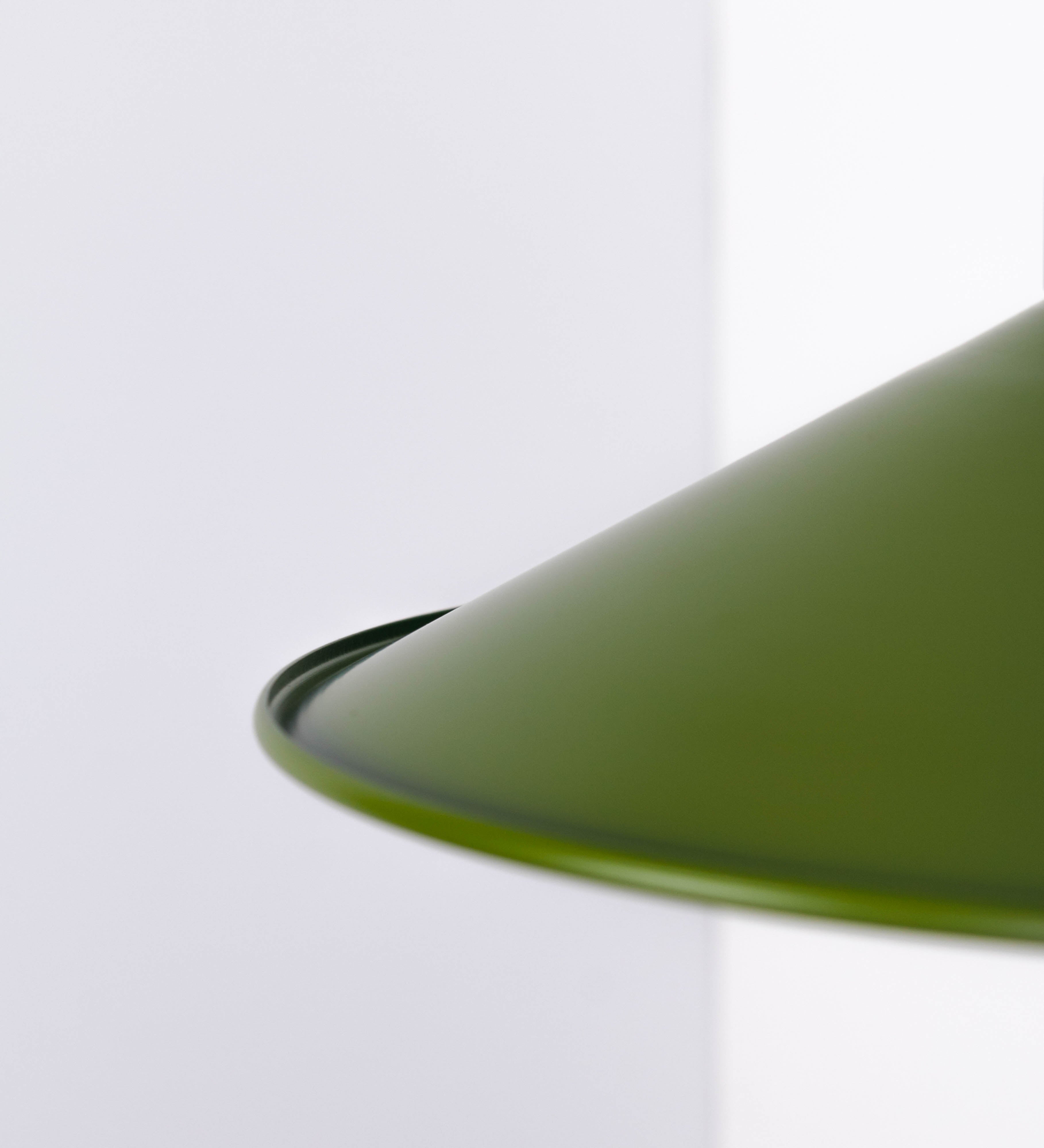 Aplique de parede com um design clássico e cores contemporâneas. O aplique é composto por uma base circular verde couve-de-bruxelas, de onde se estende um braço curvo, que forma um arco gracioso e sustenta o chapéu do candeeiro, verde também. O chapéu tem um formato cónico invertido, com uma borda ligeiramente levantada, que direciona a luz para baixo. O interior do chapéu é branco. No topo do chapéu, há um suporte circular em níquel escovado, com três braços que fixa o chapéu ao braço curvo.