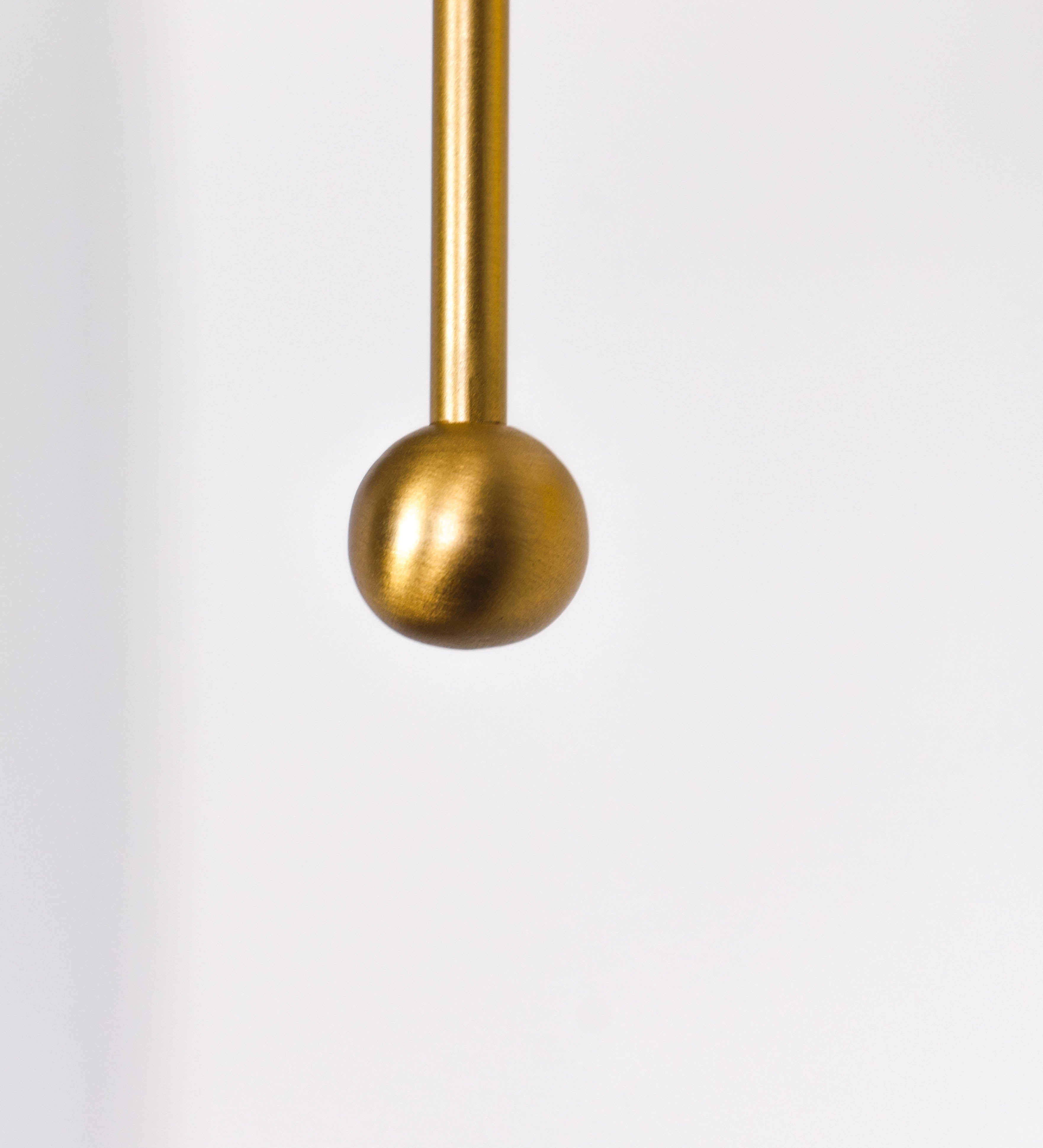 Aplique de parede com um design elegante e funcional. O aplique é todo em latão escovado. A base do aplique é redonda e fixa-se diretamente na parede. Do centro da sua base sai o braço do aplique, que é reto e horizontal. O braço é ajustável permitindo direcionar a luz. No final do braço, há um chapéu longo e arredondado e com uma pequena haste com uma esfera na ponta, que auxilia a movimentar o chapéu. O interior do chapéu é branco.