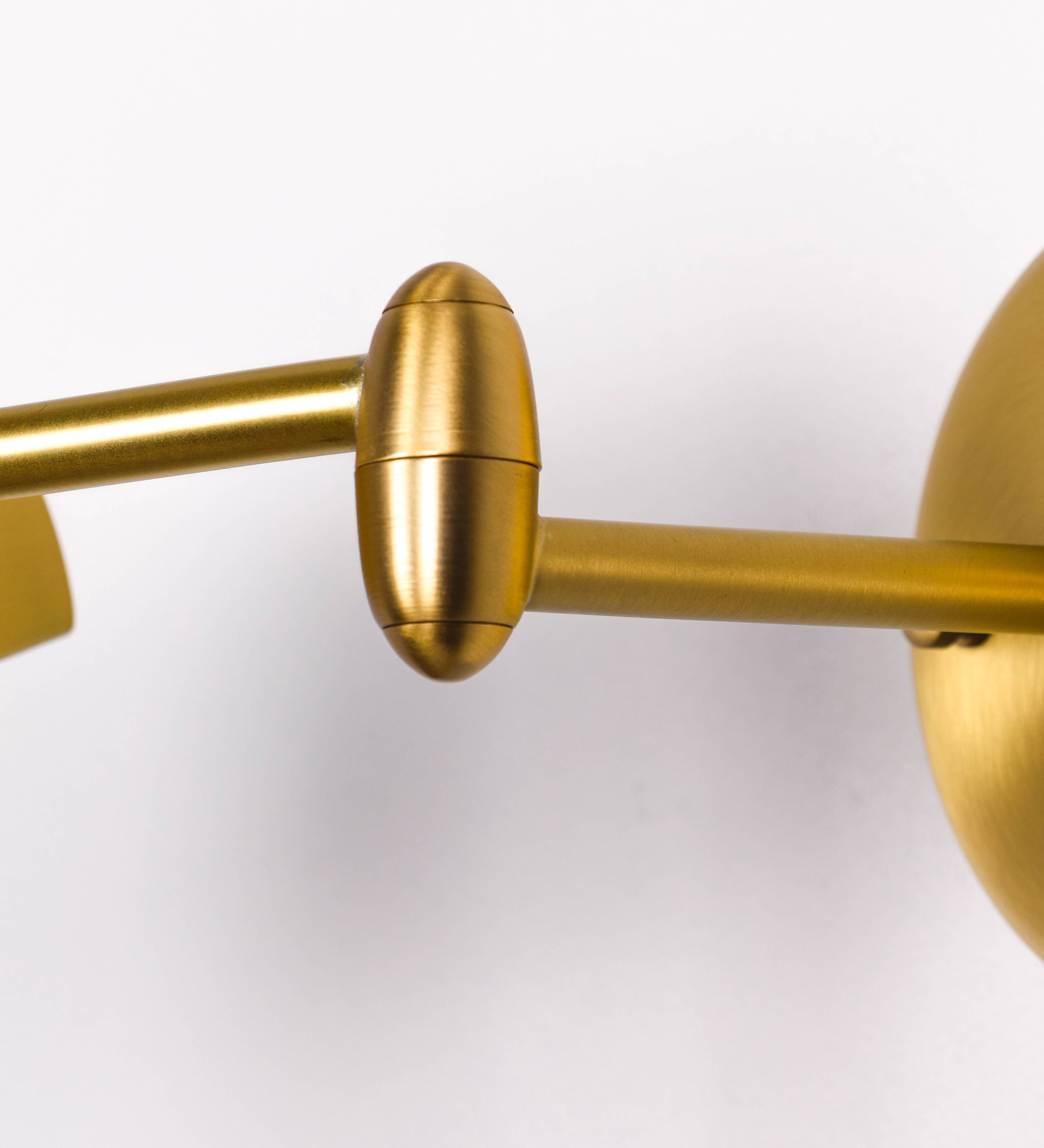 Aplique de parede com um design elegante e funcional. O aplique é todo em latão escovado. A base do aplique é redonda e fixa-se diretamente na parede. Do centro da sua base sai o braço do aplique, que é reto e horizontal. O braço é ajustável permitindo direcionar a luz. No final do braço, há um chapéu longo e arredondado e com uma pequena haste com uma esfera na ponta, que auxilia a movimentar o chapéu. O interior do chapéu é branco.