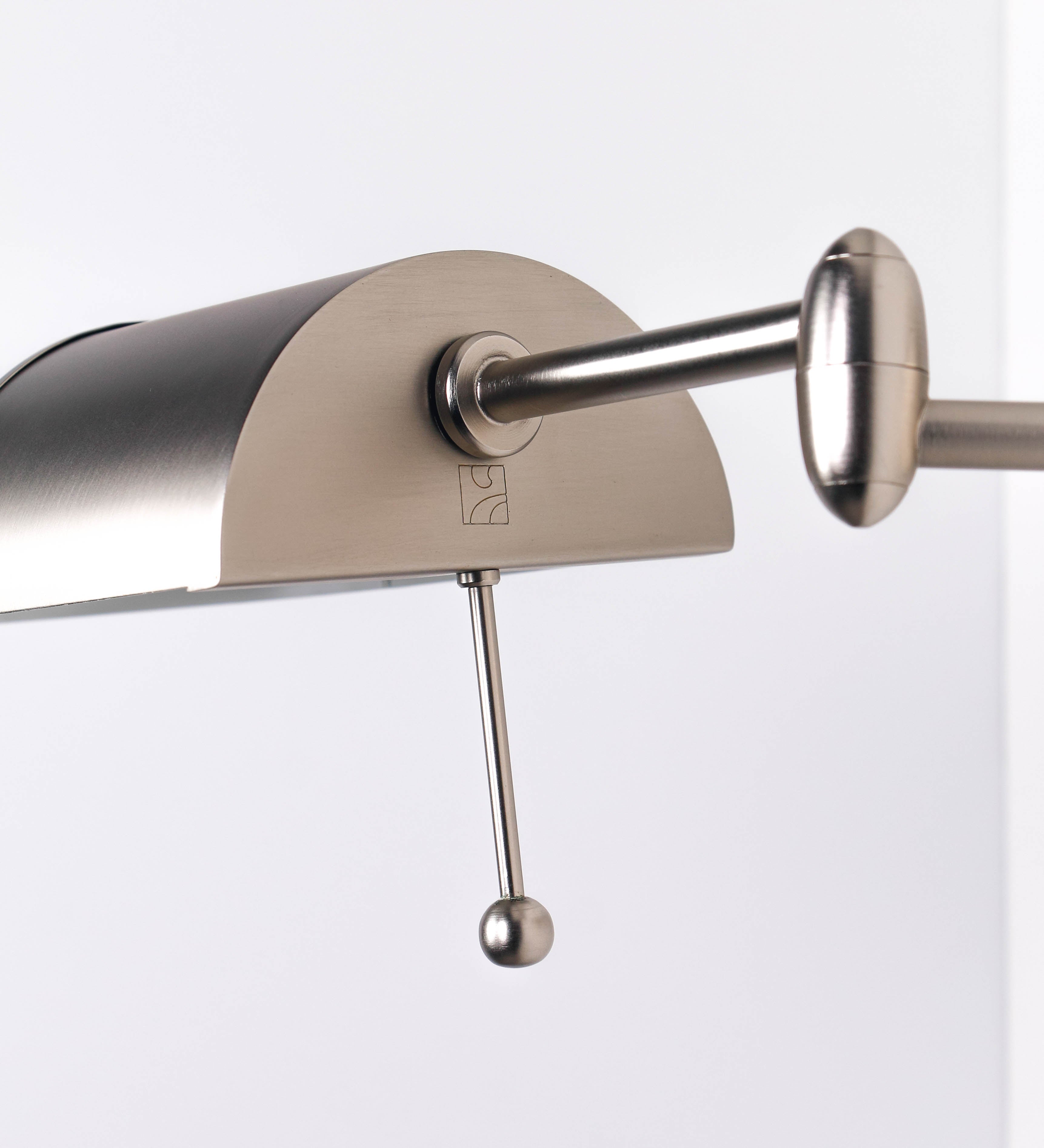 Aplique de parede com um design elegante e funcional. O aplique é todo em níquel escovado. A base do aplique é redonda e fixa-se diretamente na parede. Do centro da sua base sai o braço do aplique, que é reto e horizontal. O braço é ajustável permitindo direcionar a luz. No final do braço, há um chapéu longo e arredondado e com uma pequena haste com uma esfera na ponta, que auxilia a movimentar o chapéu. O interior do chapéu é branco.