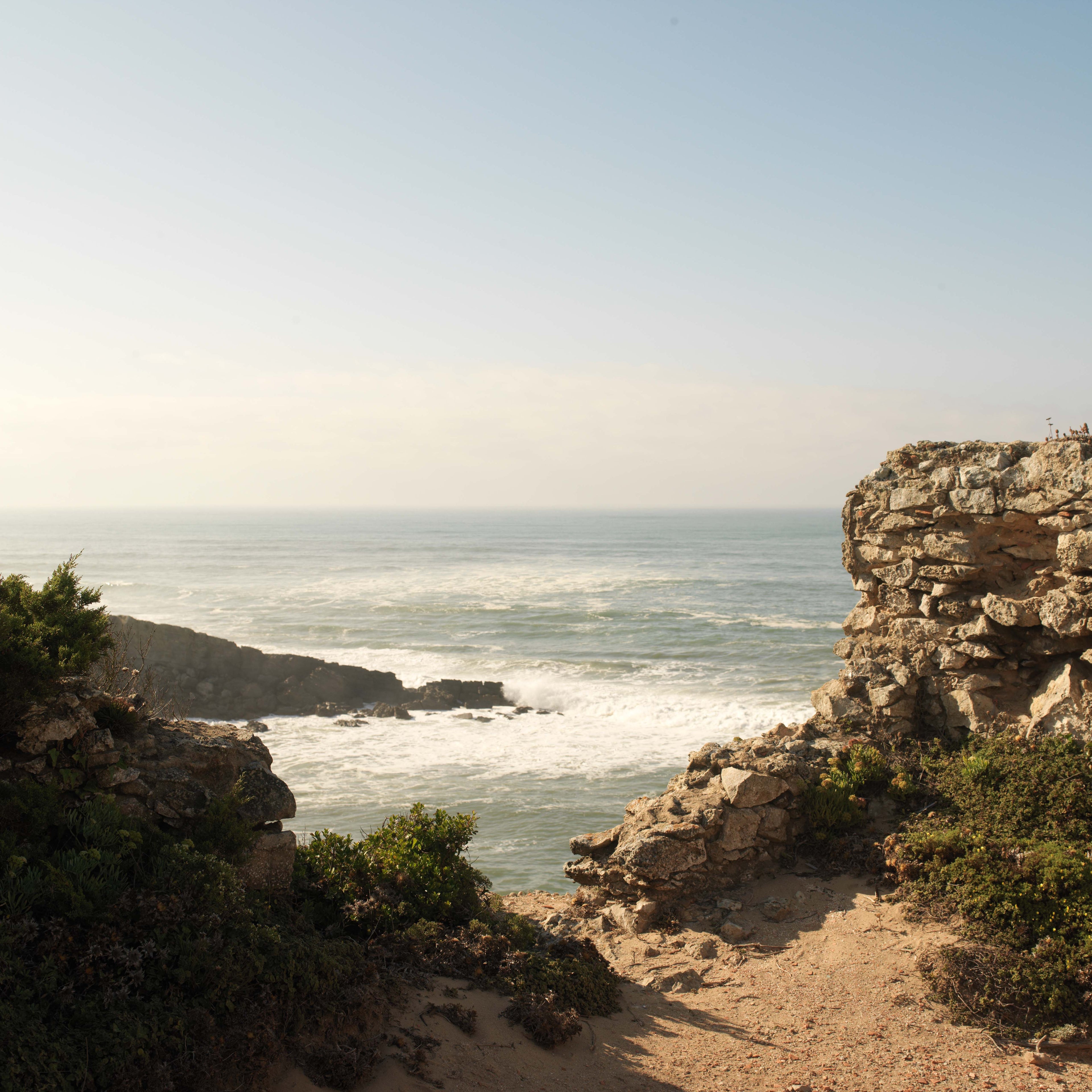 Vista costeira em Portugal com rochedos e o oceano Atlântico ao fundo.
