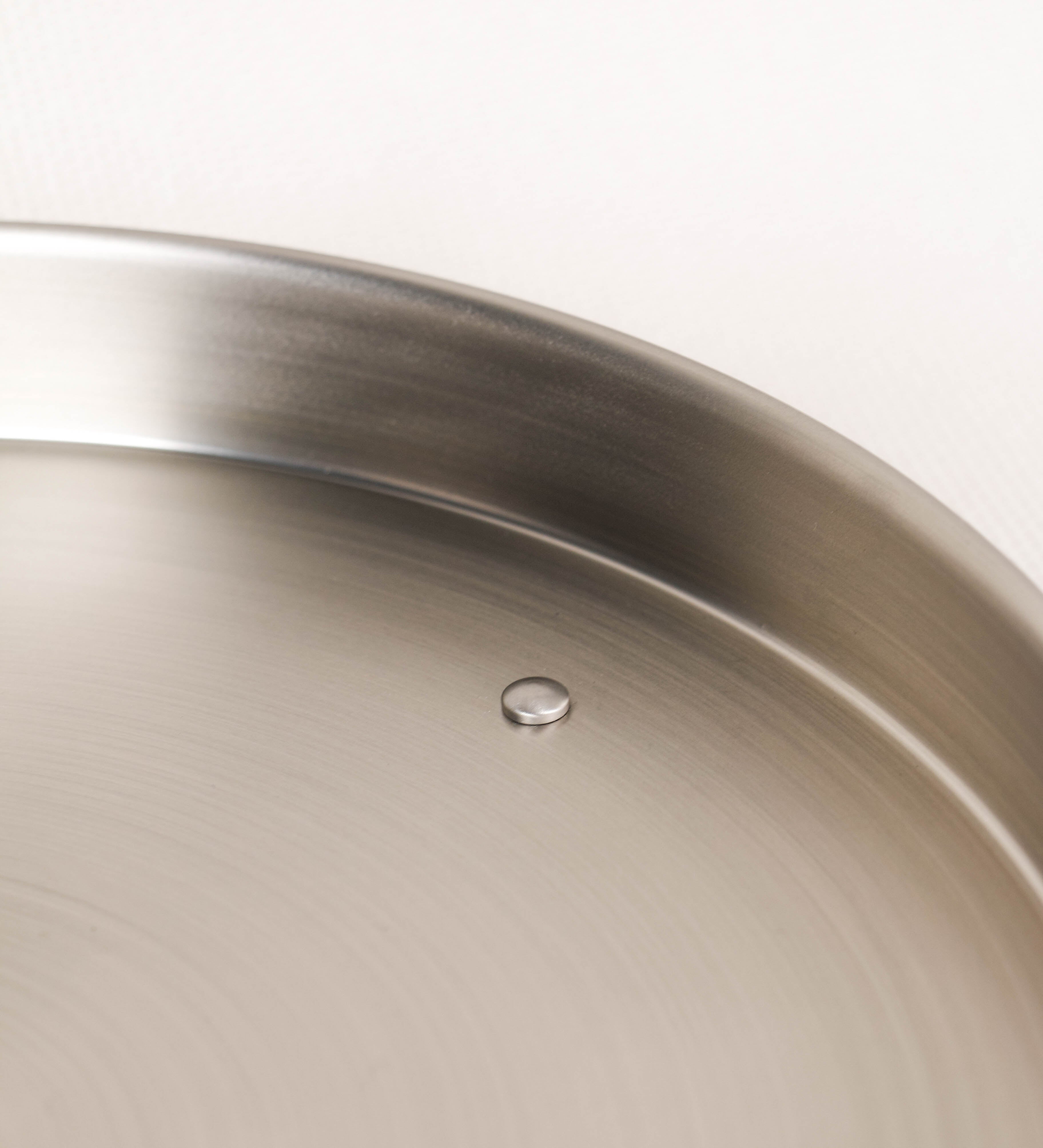 Bandeja com um design sofisticado e intemporal. A bandeja é de latão, tendo na superfície exterior um acabamento em tom prateado e com efeito de espelho, e um acabamento em tom prateado com efeito mate na superfície interior. Tem uma forma circular, de superfície plana e com uma borda envolvente de altura média e grossura fina. Na sua base tem três pequenas esferas, em níquel polido também, dispostas em formato triangular, que sustentam o prato circular no topo.