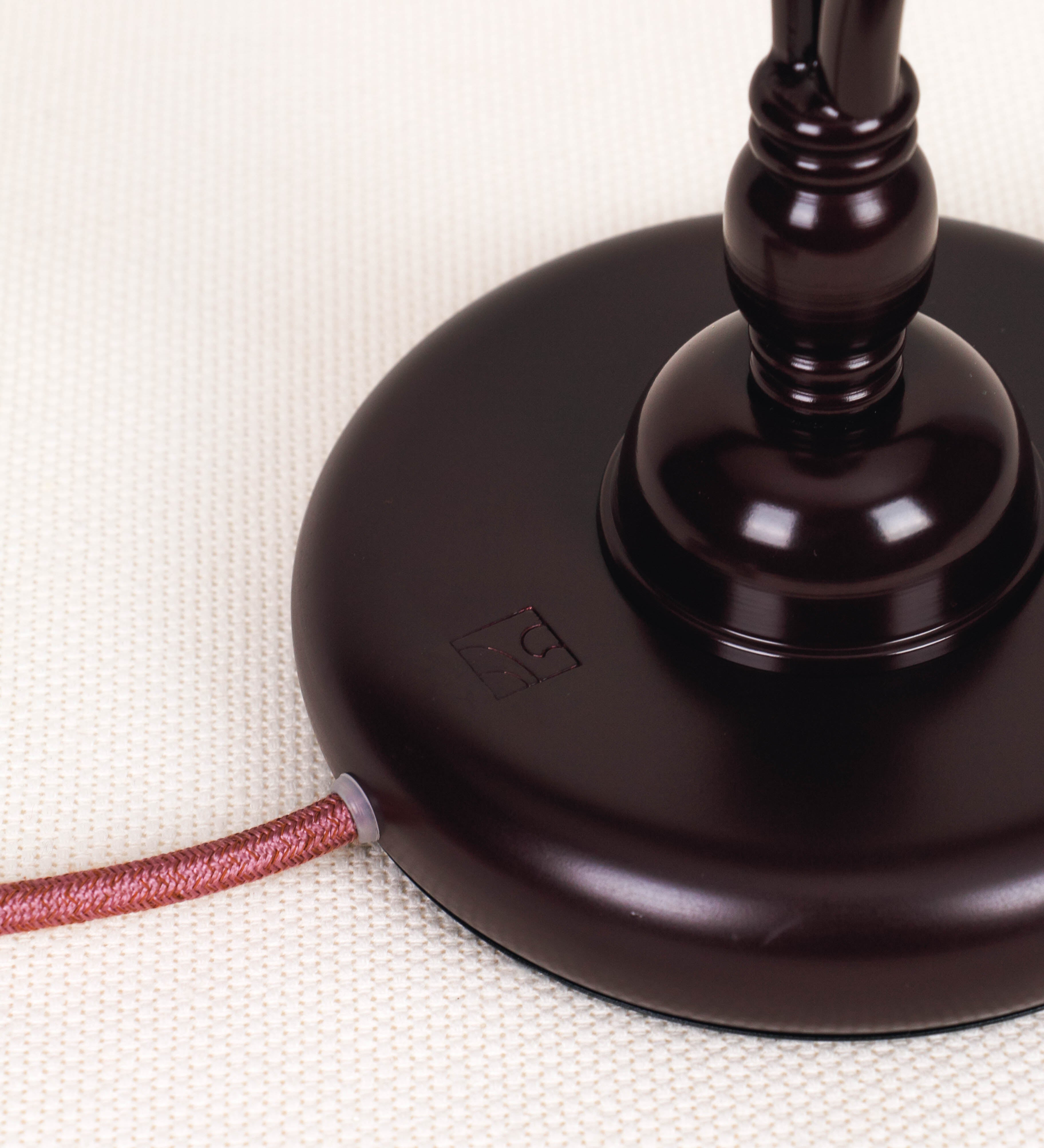 Candeeiro de mesa com um design clássico e sofisticado. O candeeiro possui uma base circular e robusta de tom vinho. A estrutura da base é complementada por um suporte em forma de nó, também de tom vinho, que se eleva graciosamente até ao suporte da luz. A luz é difundida através de uma esfera de vidro fosco branco, assente no corpo. O cabo é revestido têxtil de tom rosa velho, com interruptor e ficha transparentes.