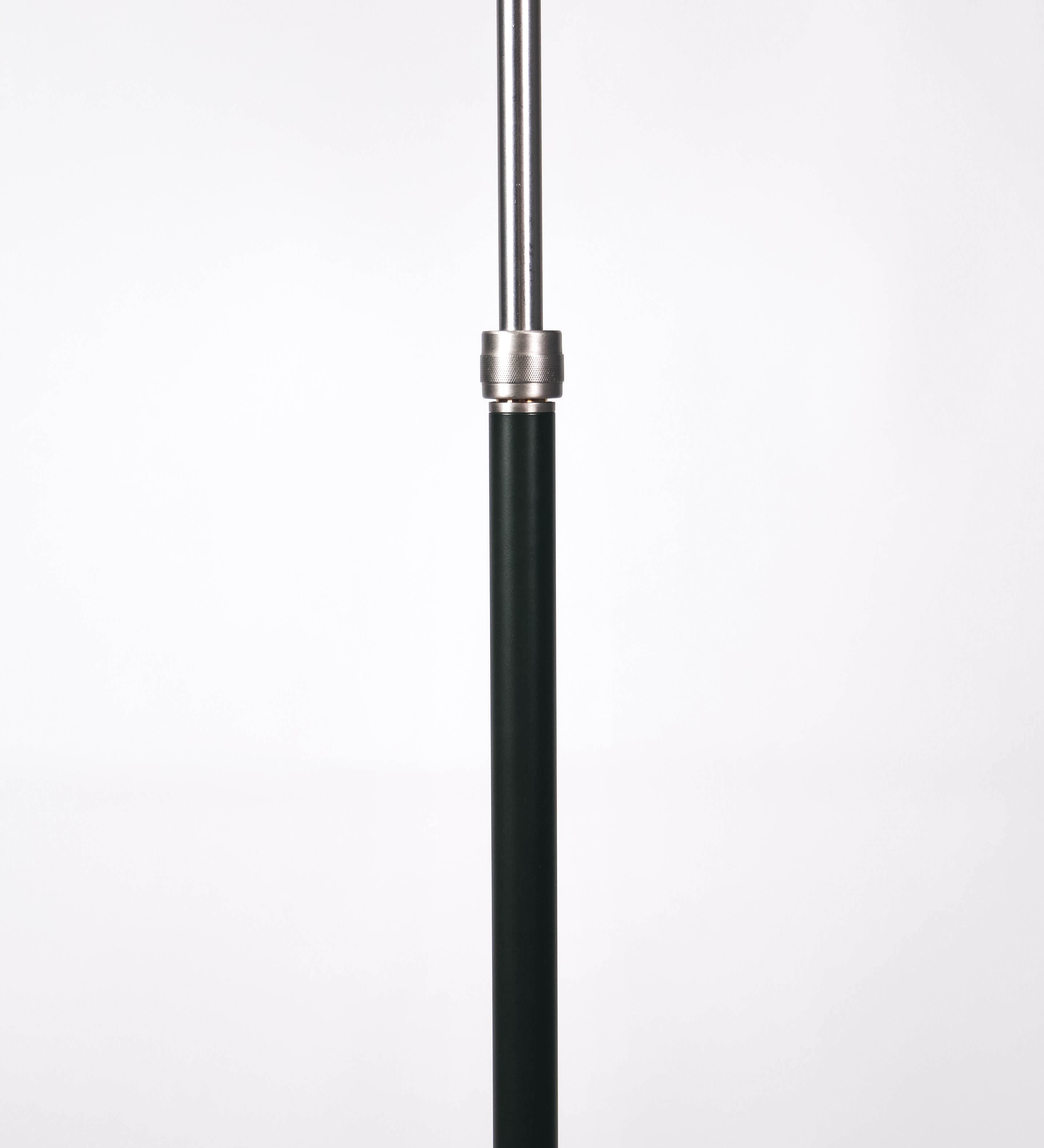 Candeeiro de pé com base circular em verde-azeitona. O corpo é fino e vertical, composto por uma haste verde-azeitona, e uma outra haste em níquel escovado, que permite ajustar a altura do candeeiro. A haste ajustável conecta a um braço horizontal, que sustenta o chapéu, e é manipulável. O chapéu é longo e arredondado, em verde-azeitona, e com uma pequena haste com uma esfera na ponta. O interior do chapéu é branco. O cabo é revestido têxtil em preto, com um interruptor de pé preto circular.