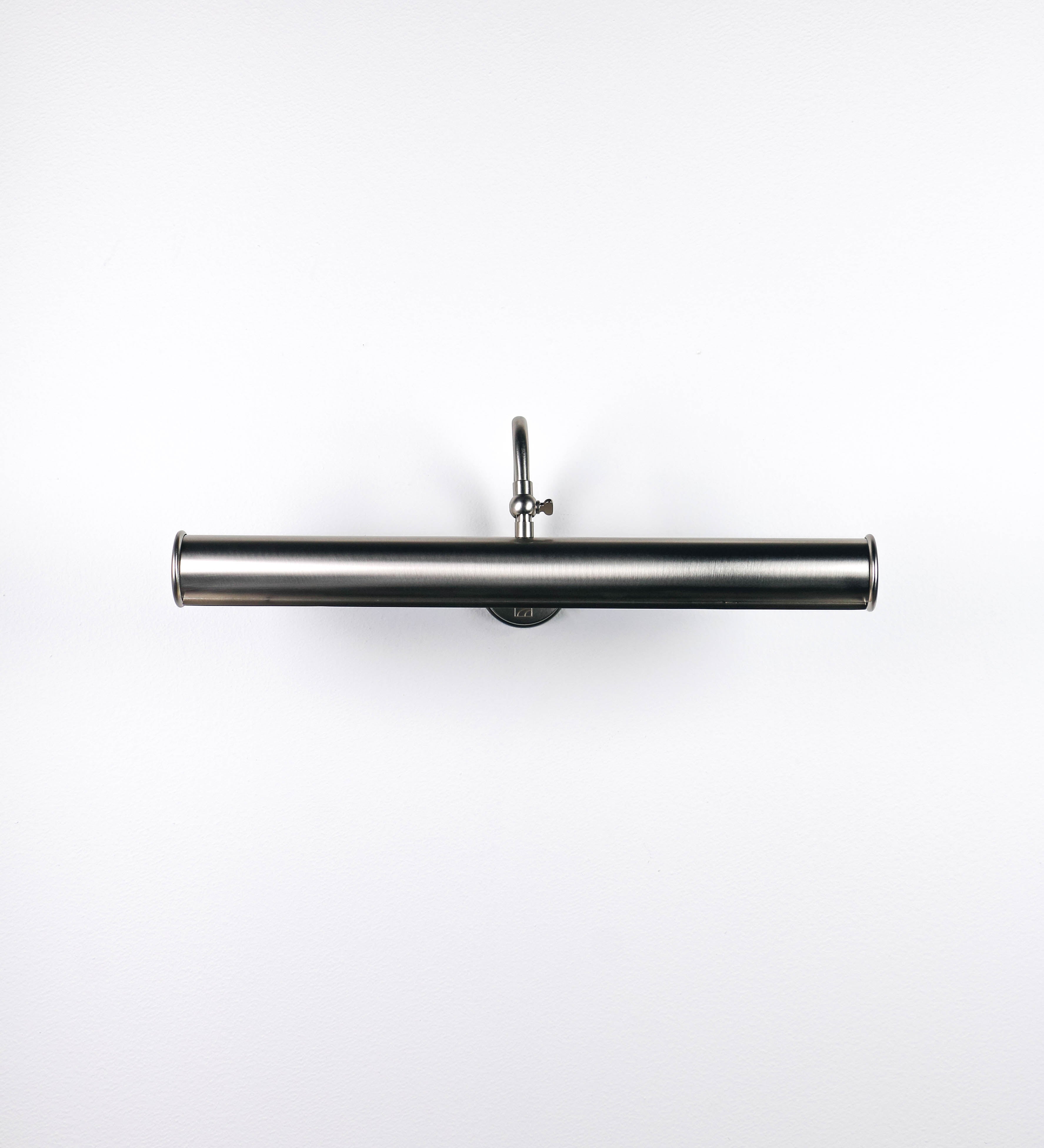 Aplique de parede que combina elementos clássicos com toques contemporâneos, todo em níquel escovado. O aplique é composto por uma base circular de onde se estende um braço curvo e gracioso, que suporta a barra principal. O braço contém um elemento que permite apertar ou desapertar a barra para melhor manipular a direção da luz. A barra de 45cm de largura é cilíndrica e alongada. As extremidades do cilindro são planas e do mesmo diâmetro.
