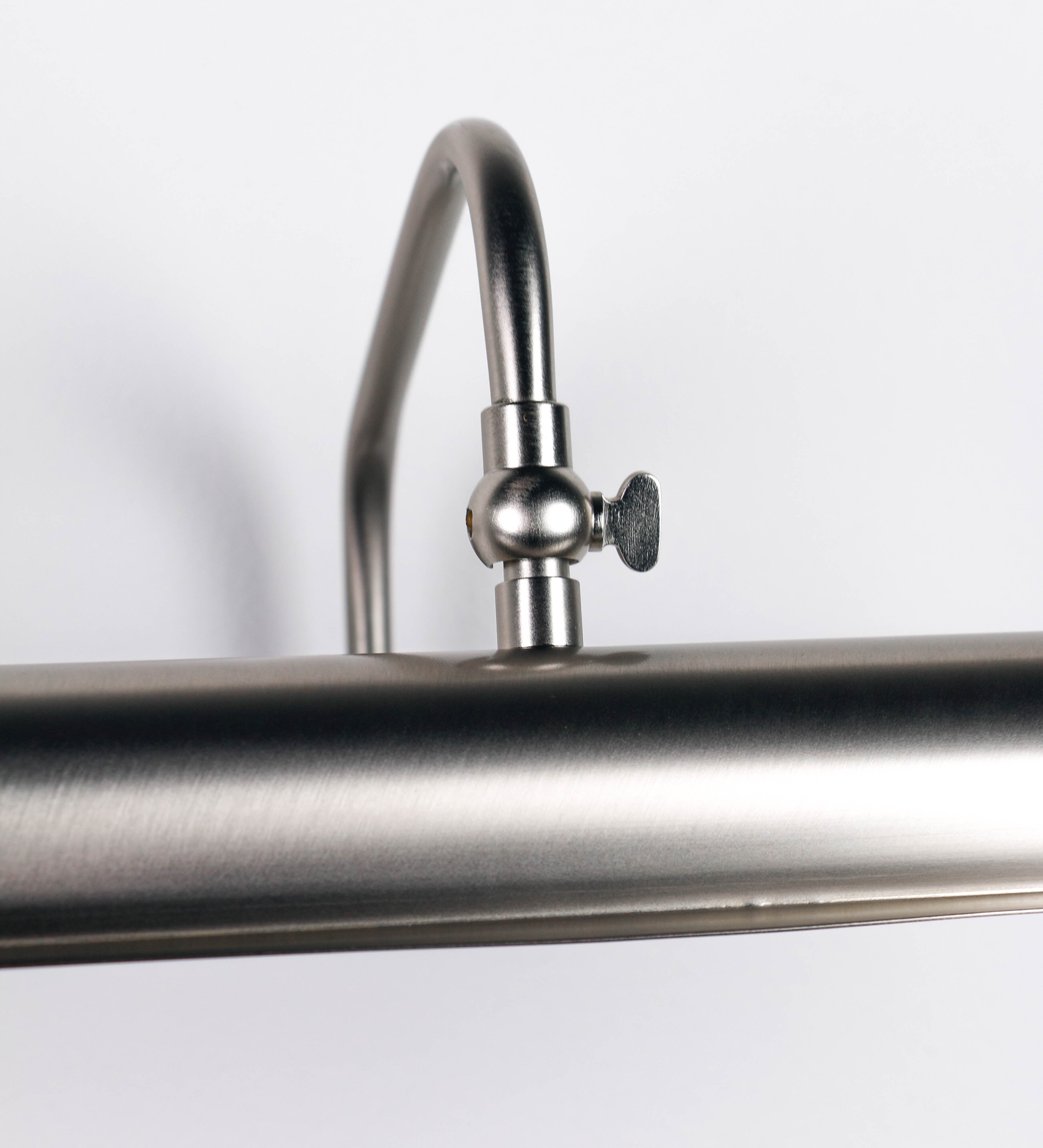Aplique de parede que combina elementos clássicos com toques contemporâneos, todo em níquel escovado. O aplique é composto por uma base retangular, de onde se estendem dois braços curvos e graciosos, que suportam a barra principal. Os braços contêm um elemento que permite apertar ou desapertar a barra para melhor manipular a direção da luz. A barra de 65cm de largura é cilíndrica e alongada. As extremidades do cilindro são planas e do mesmo diâmetro.