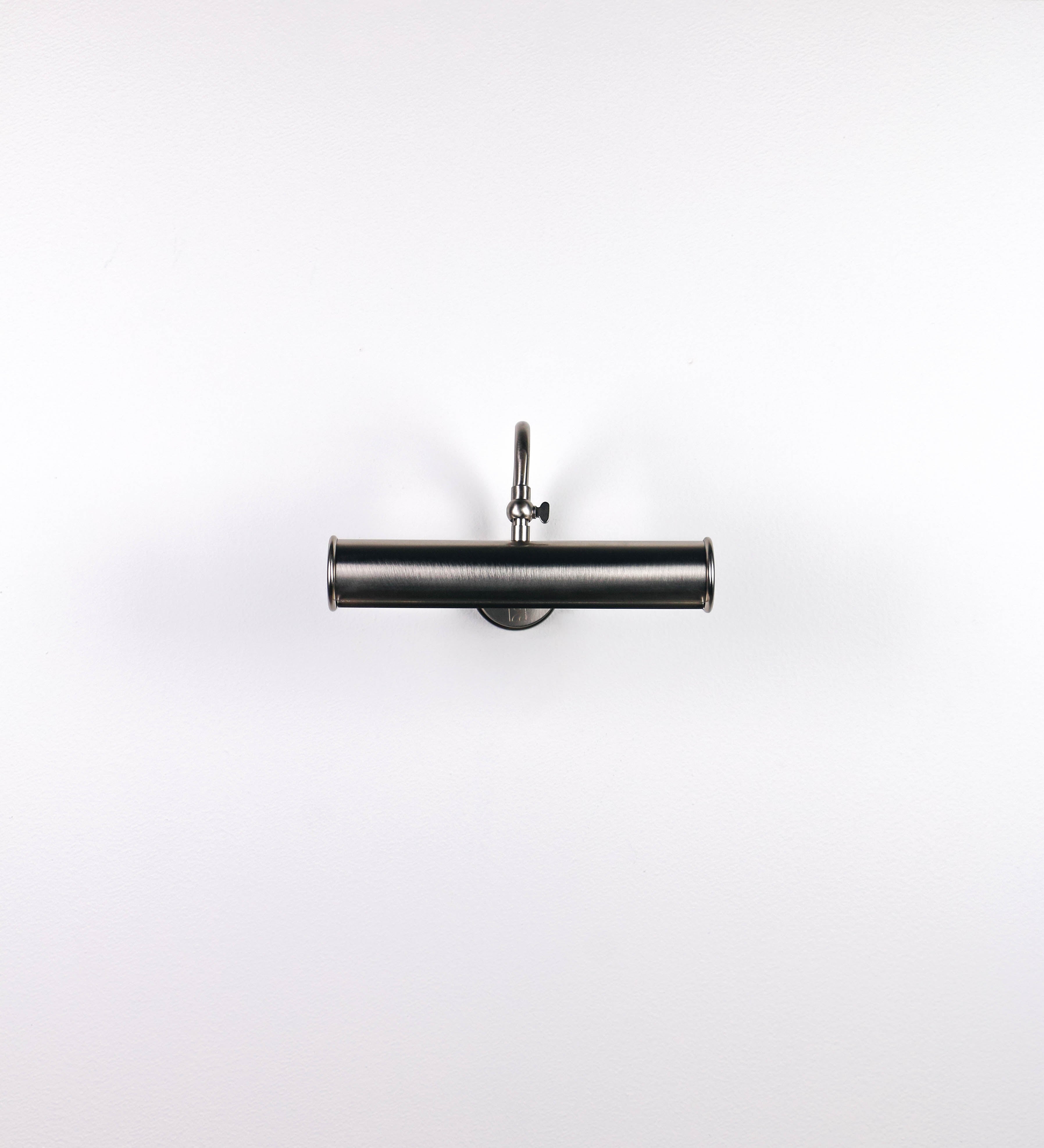 Aplique de parede que combina elementos clássicos com toques contemporâneos, todo em níquel escovado. O aplique é composto por uma base circular de onde se estende um braço curvo e gracioso, que suporta a barra principal. O braço contém um elemento que permite apertar ou desapertar a barra para melhor manipular a direção da luz. A barra de 25cm de largura é cilíndrica e alongada. As extremidades do cilindro são planas e do mesmo diâmetro.