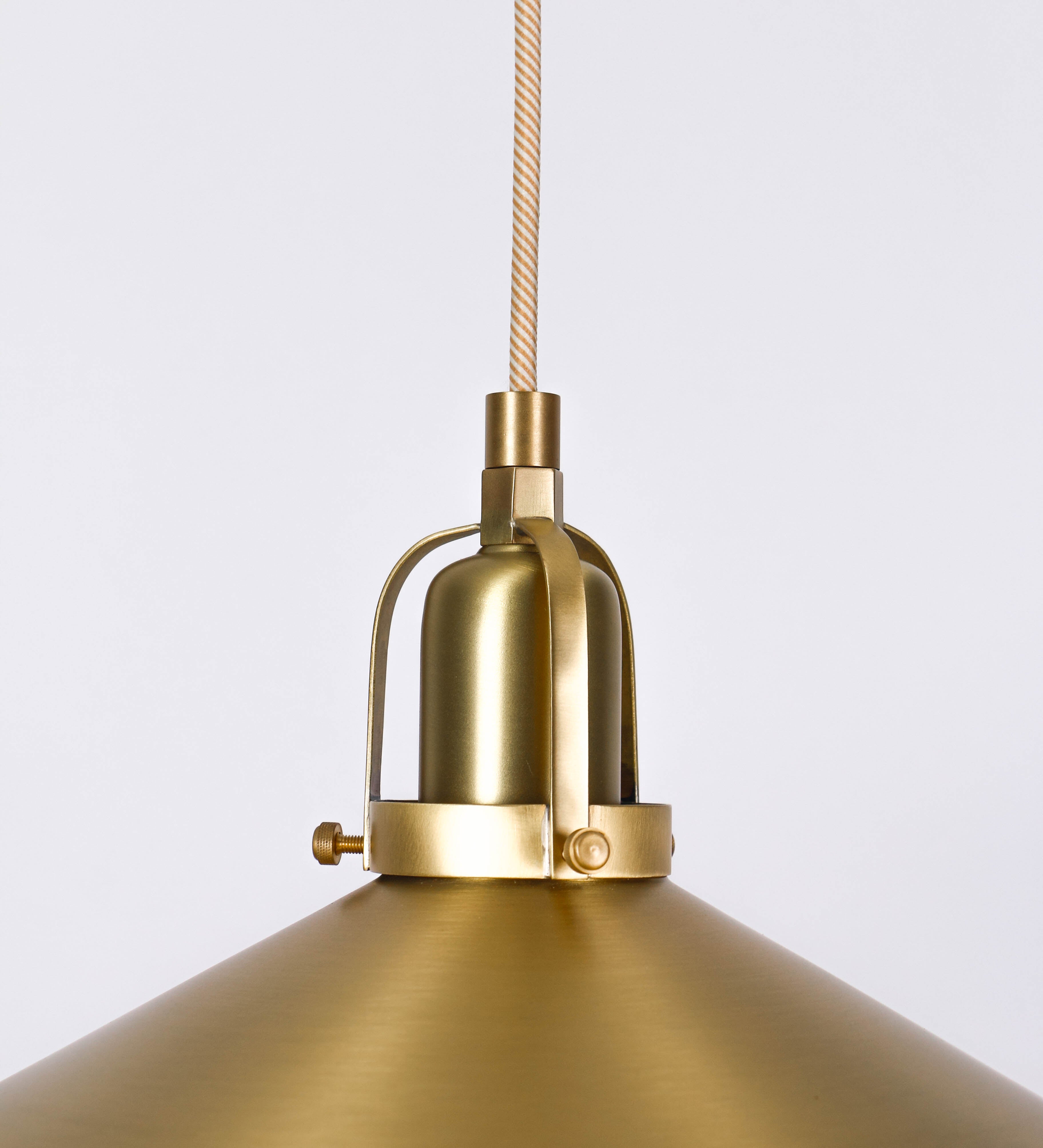 Suspensão de teto que combina um design clássico com um acabamento moderno e sofisticado. A suspensão, toda em latão escovado, é fixa ao teto através de uma base circular de onde desce um cabo revestido têxtil com um padrão trançado com linhas douradas e brancas, que sustenta o chapéu principal. O chapéu tem um formato cónico invertido, com uma borda ligeiramente levantada. No topo do chapéu, há um suporte circular com três pequenos braços que conecta o chapéu ao cabo.