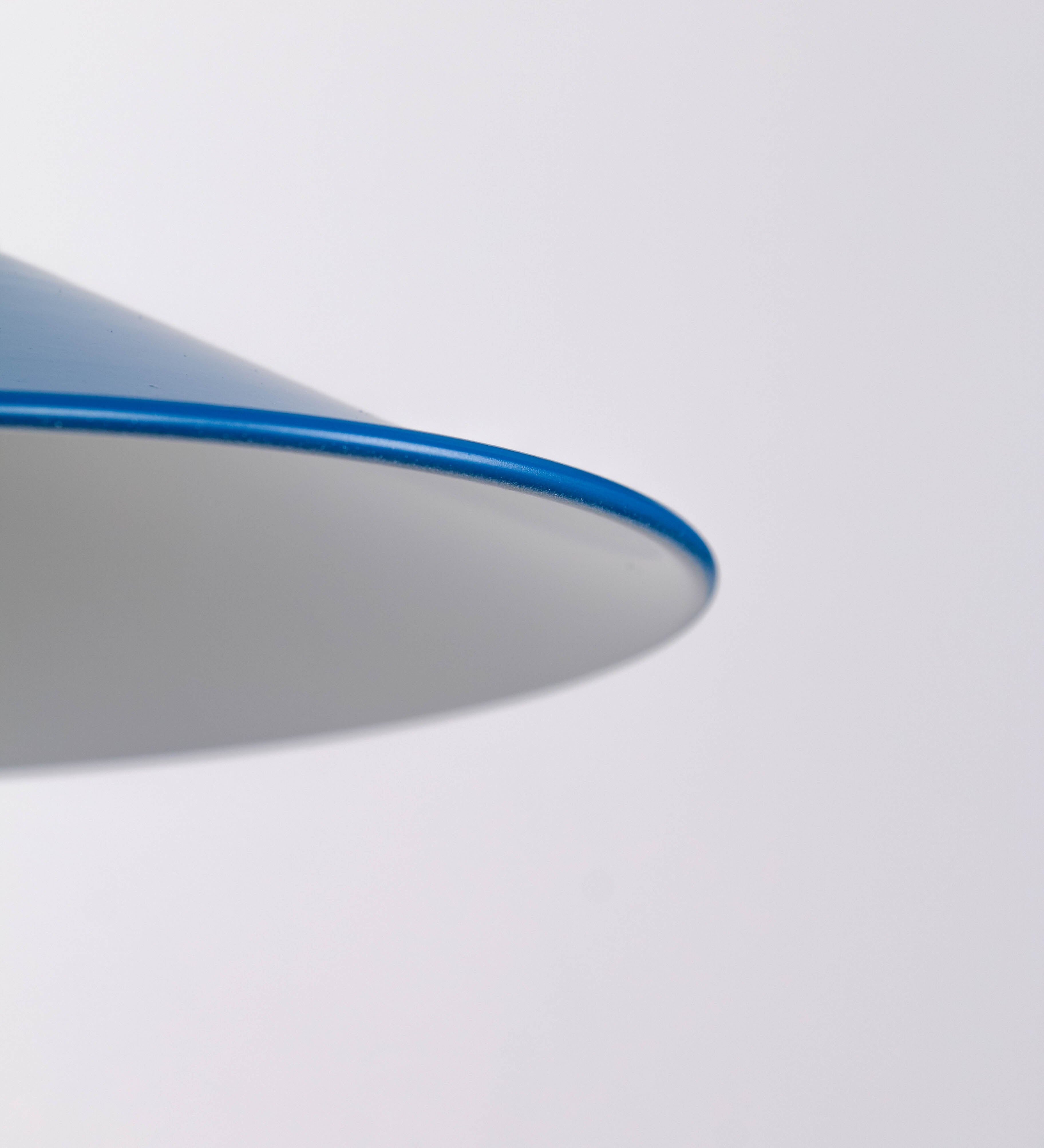 Aplique de parede com um design clássico e cores contemporâneas. O aplique é composto por uma base circular azul vintage, de onde se estende um braço curvo, que forma um arco gracioso e sustenta o chapéu do candeeiro, azul vintage também. O chapéu tem um formato cónico invertido, com uma borda ligeiramente levantada, que direciona a luz para baixo. O interior do chapéu é branco. No topo do chapéu, há um suporte circular em latão escovado, com três braços que fixa o chapéu ao braço curvo.