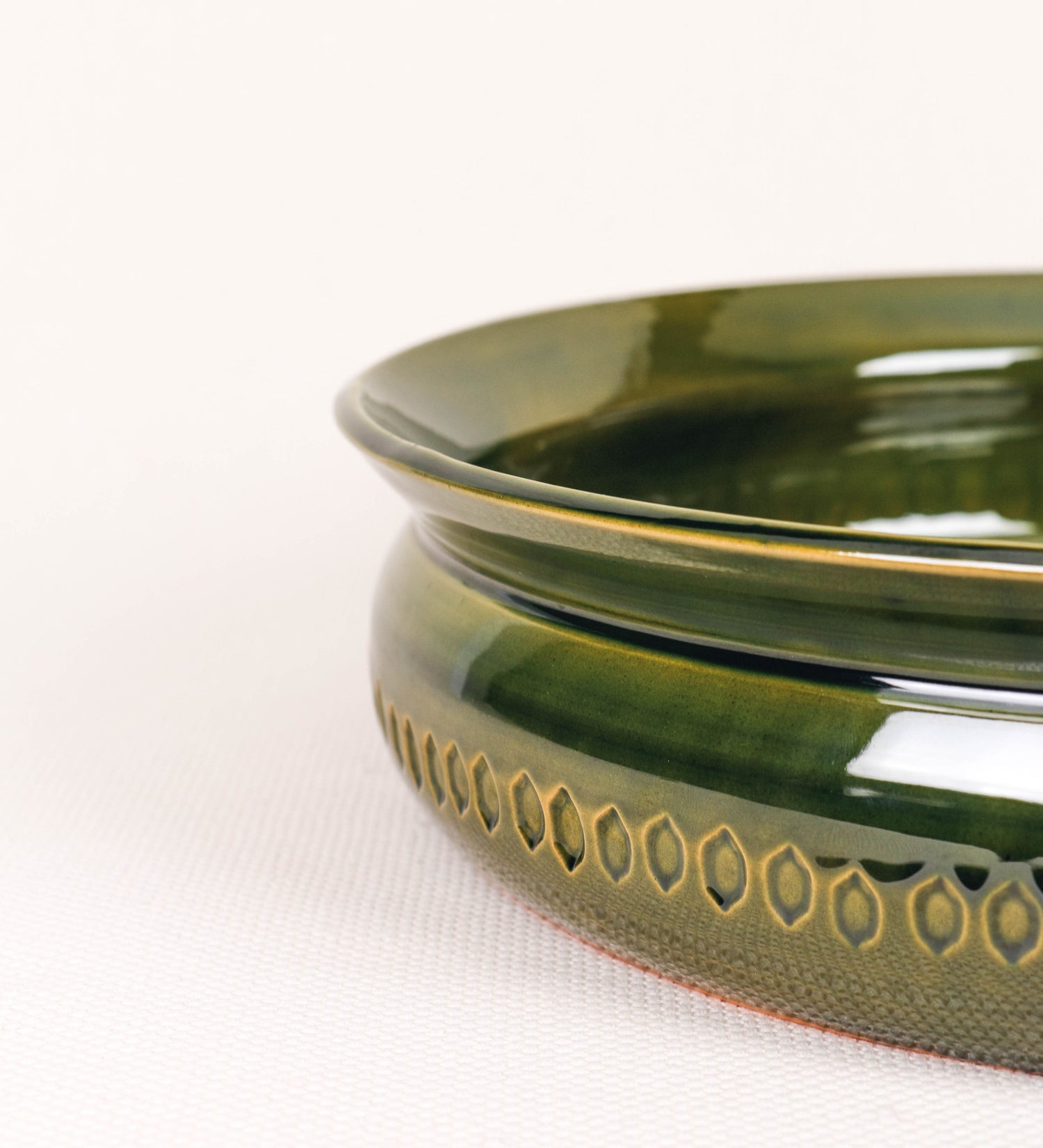 Assadeira para frangos com um design rústico e distinto. O assa-frangos é de barro, vidrado em tom verde vidro com brilho, conferindo um caráter vintage à peça. A forma do assa-frangos é circular, com uma borda superior mais estreita e um espeto cónico centrado no interior para colocar os frangos. A superfície externa da peça é decorada com um padrão de relevos losangulares, que envolvem o assa-frangos e acrescentam textura e interesse visual ao design.