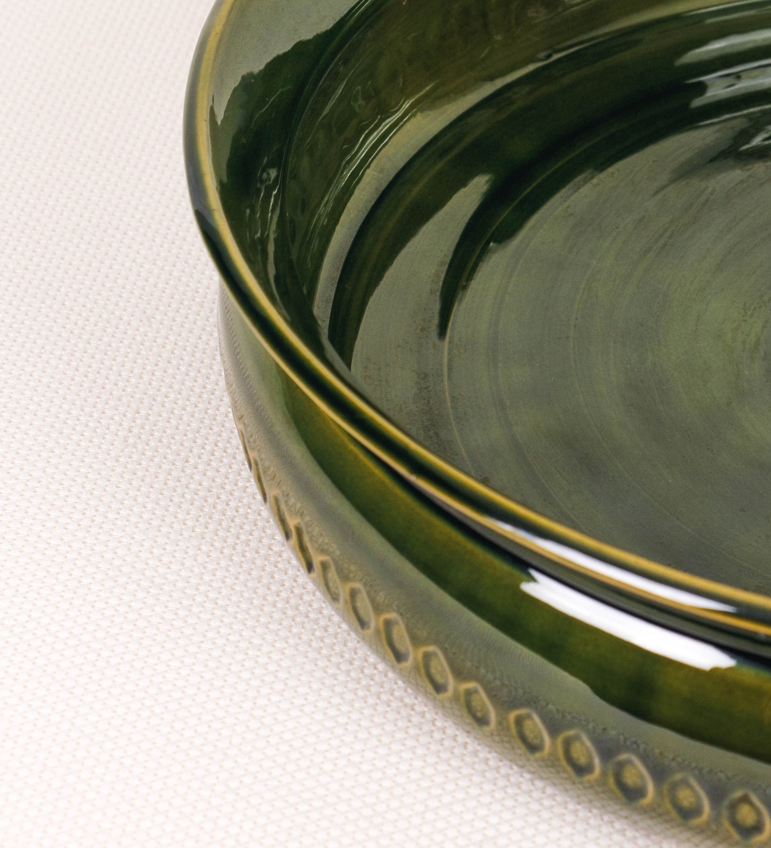 Assadeira para frangos com um design rústico e distinto. O assa-frangos é de barro, vidrado em tom verde vidro com brilho, conferindo um caráter vintage à peça. A forma do assa-frangos é circular, com uma borda superior mais estreita e um espeto cónico centrado no interior para colocar os frangos. A superfície externa da peça é decorada com um padrão de relevos losangulares, que envolvem o assa-frangos e acrescentam textura e interesse visual ao design.