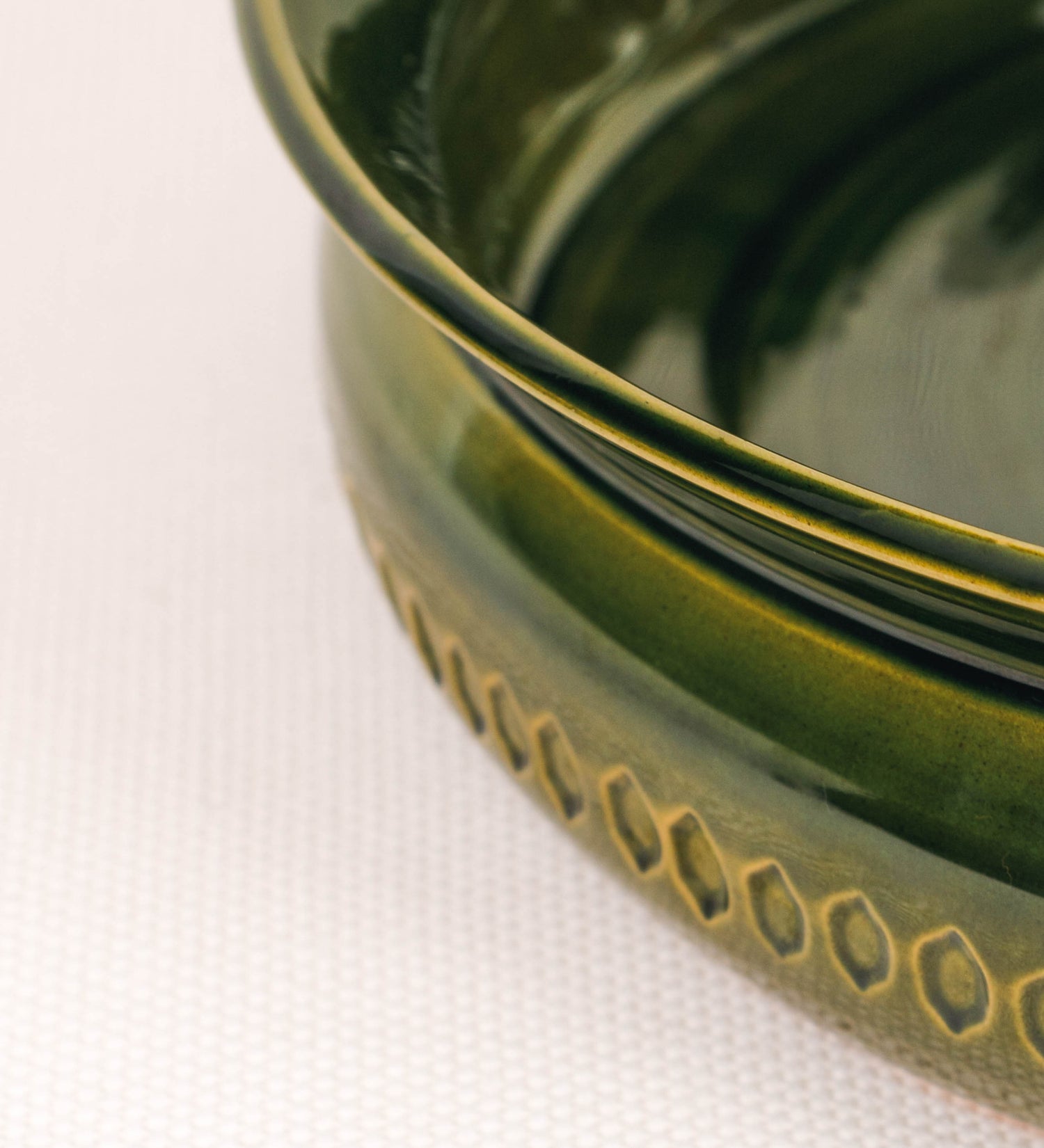 Assadeira para frangos com um design rústico e distinto. O assa-frangos é de barro, vidrado em tom verde vidro com brilho, conferindo um caráter vintage à peça. A forma do assa-frangos é circular, com uma borda superior mais estreita e um espeto cónico centrado no interior para colocar os frangos. A superfície externa da peça é decorada com um padrão de relevos losangulares, que envolvem o assa-frangos e acrescentam textura e interesse visual ao design.