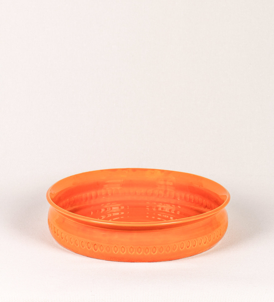 Assadeira com um design rústico e distinto. A assadeira é de barro, vidrado em tom laranja tangerina com brilho, conferindo um caráter chamativo à peça. A forma da assadeira é circular, com uma borda superior mais estreita. A superfície externa da peça é decorada com um padrão de relevos losangulares, que envolvem a assadeira e acrescentam textura e interesse visual ao design.
