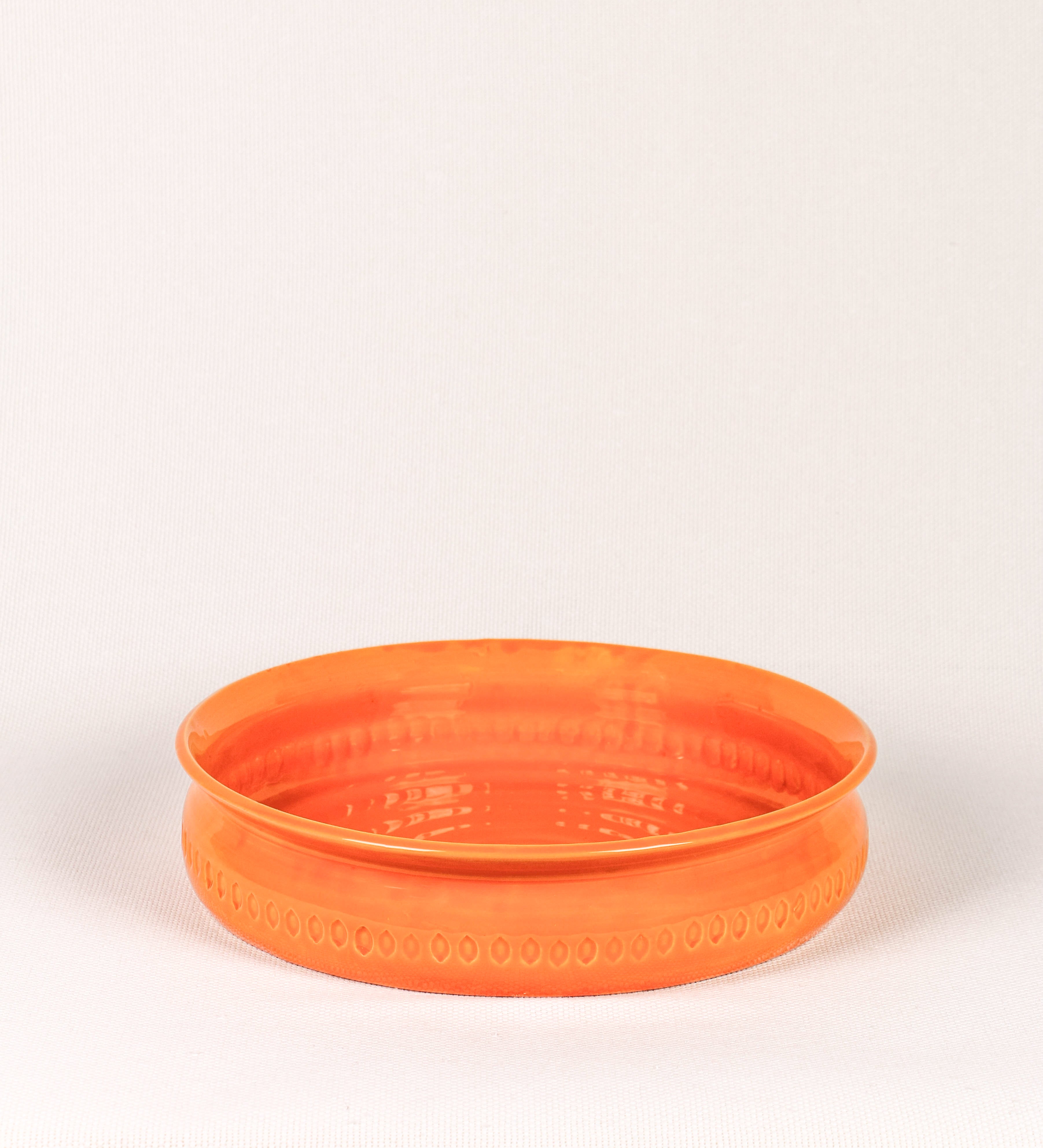 Assadeira com um design rústico e distinto. A assadeira é de barro, vidrado em tom laranja tangerina com brilho, conferindo um caráter chamativo à peça. A forma da assadeira é circular, com uma borda superior mais estreita. A superfície externa da peça é decorada com um padrão de relevos losangulares, que envolvem a assadeira e acrescentam textura e interesse visual ao design.