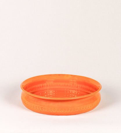 Assadeira com um design rústico e distinto. A assadeira é de barro, vidrado em tom laranja tangerina com brilho, conferindo um caráter chamativo à peça. A forma da assadeira é circular, com uma borda superior mais estreita. A superfície externa da peça é decorada com um padrão de relevos losangulares, que envolvem a assadeira e acrescentam textura e interesse visual ao design.