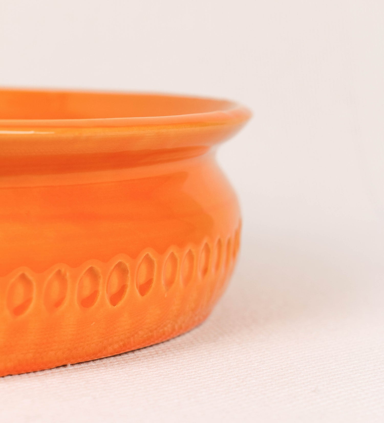 Assadeira com um design rústico e distinto. A assadeira é de barro, vidrado em tom laranja tangerina com brilho, conferindo um caráter chamativo à peça. A forma da assadeira é circular, com uma borda superior mais estreita. A superfície externa da peça é decorada com um padrão de relevos losangulares, que envolvem a assadeira e acrescentam textura e interesse visual ao design.