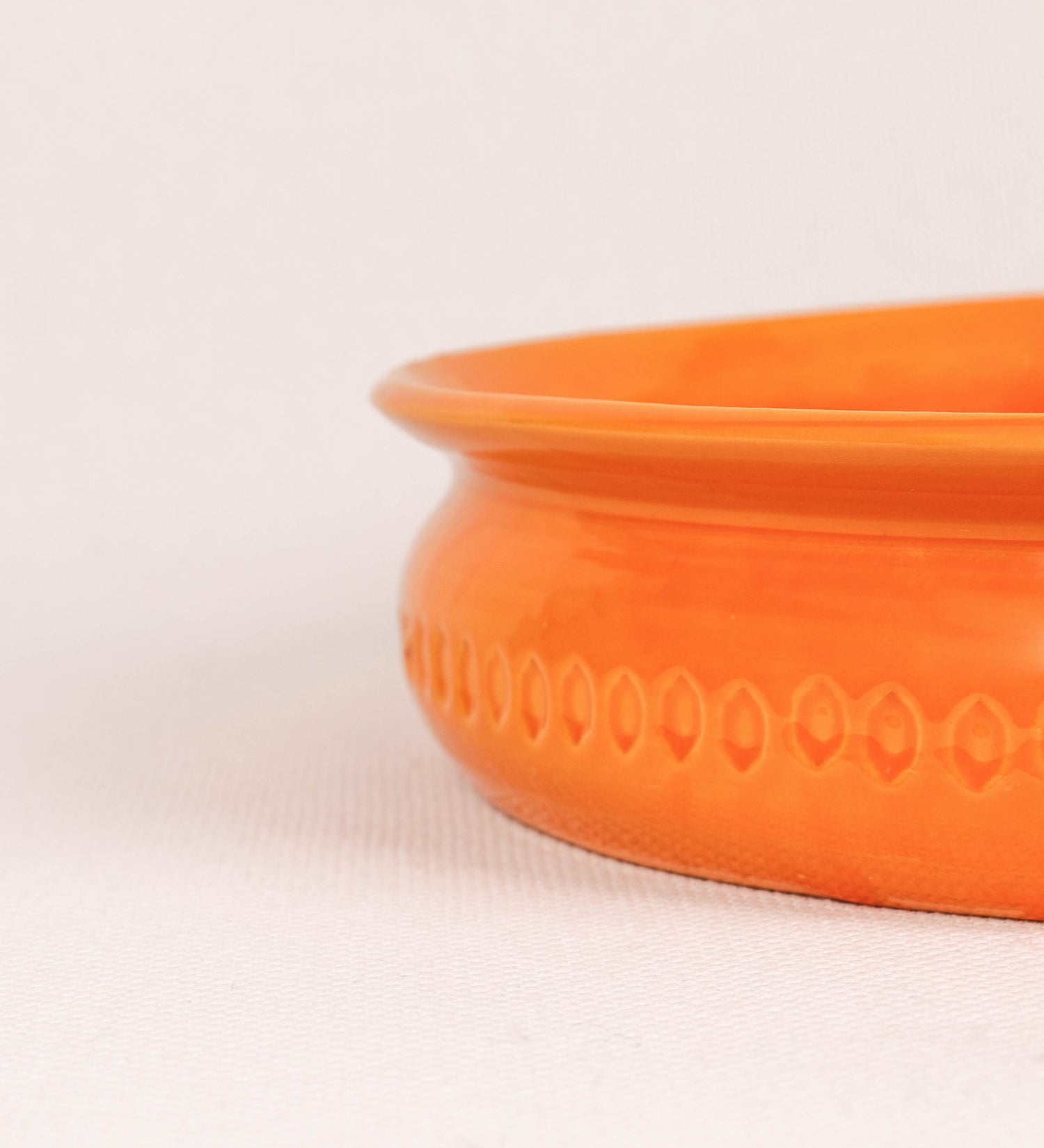 Assadeira com um design rústico e distinto. A assadeira é de barro, vidrado em tom laranja tangerina com brilho, conferindo um caráter chamativo à peça. A forma da assadeira é circular, com uma borda superior mais estreita. A superfície externa da peça é decorada com um padrão de relevos losangulares, que envolvem a assadeira e acrescentam textura e interesse visual ao design.