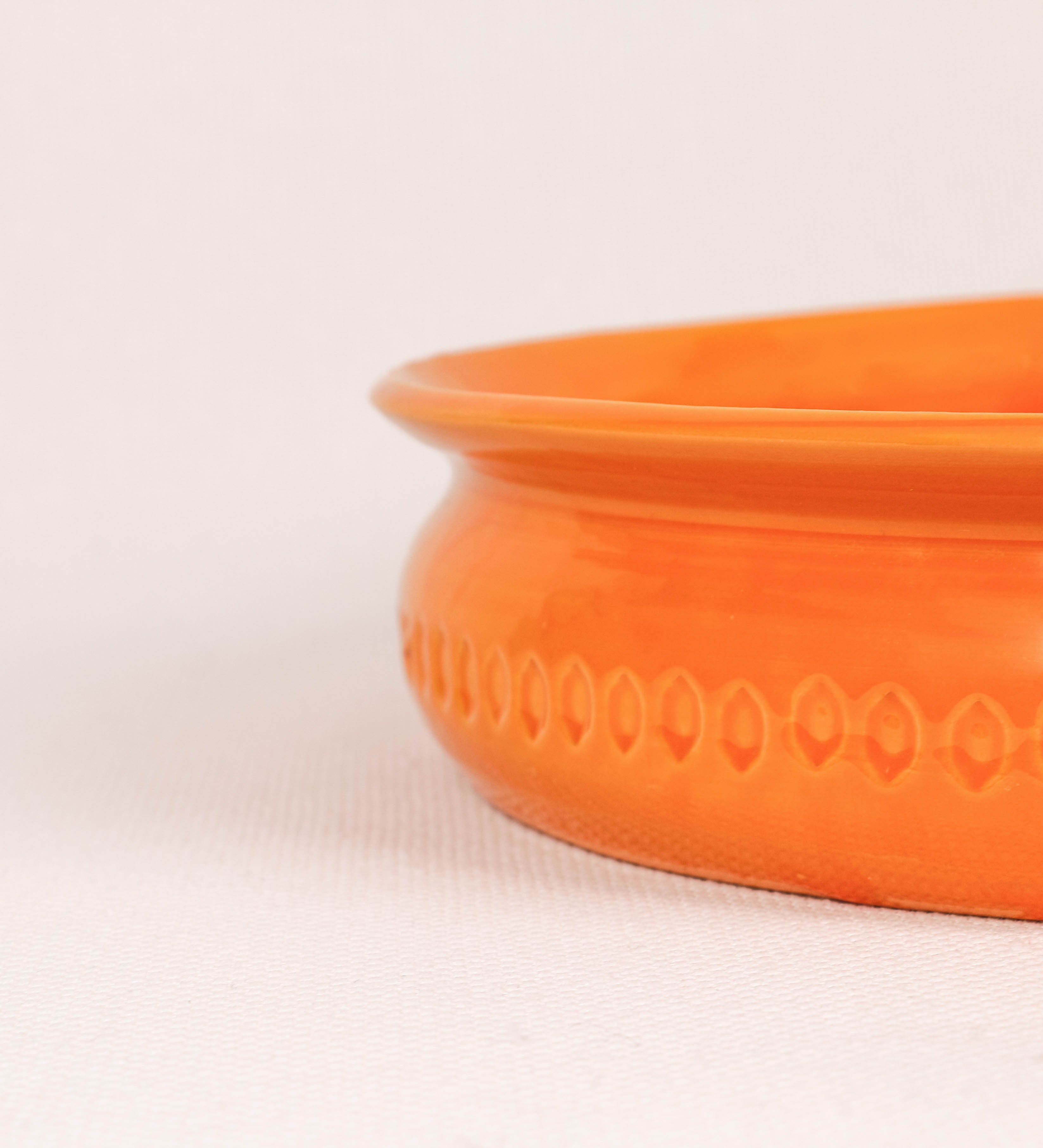 Assadeira com um design rústico e distinto. A assadeira é de barro, vidrado em tom laranja tangerina com brilho, conferindo um caráter chamativo à peça. A forma da assadeira é circular, com uma borda superior mais estreita. A superfície externa da peça é decorada com um padrão de relevos losangulares, que envolvem a assadeira e acrescentam textura e interesse visual ao design.