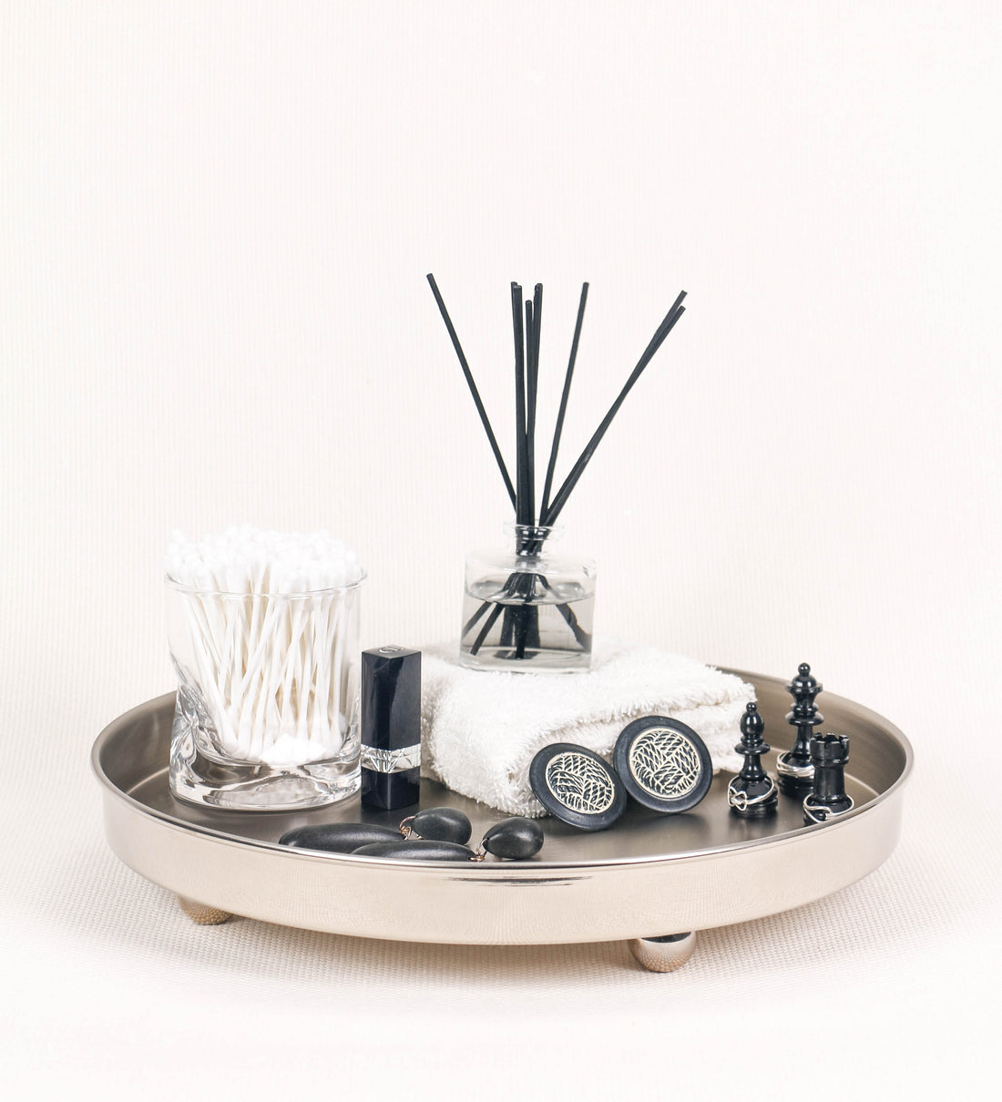 Bandeja com um design sofisticado e intemporal. A bandeja é de latão, tendo na superfície exterior um acabamento em tom prateado e com efeito de espelho, e um acabamento em tom prateado com efeito mate na superfície interior. Tem uma forma circular, de superfície plana e com uma borda envolvente de altura média e grossura fina. Na sua base tem três pequenas esferas, em níquel polido também, dispostas em formato triangular, que sustentam o prato circular no topo. 