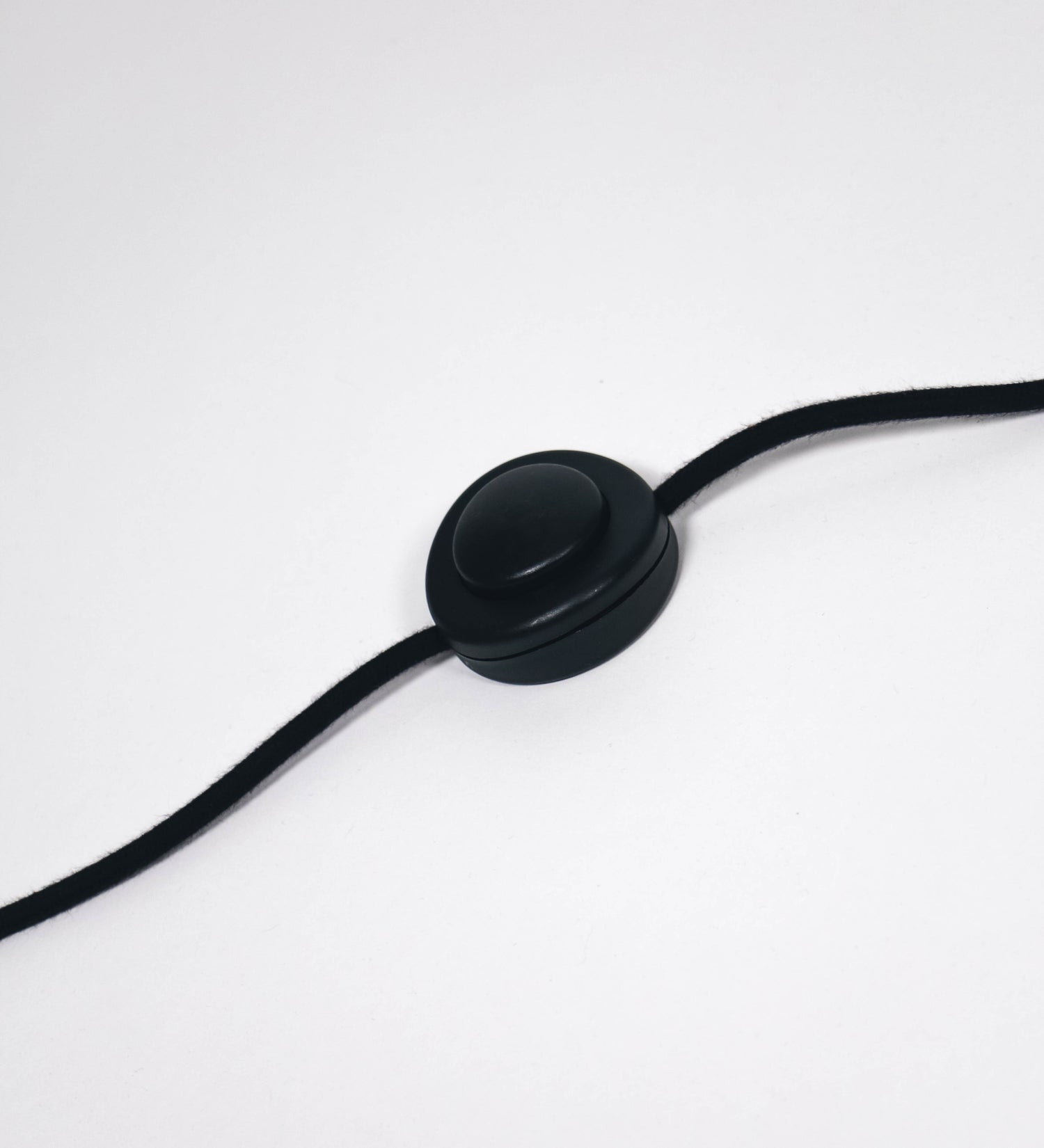 Cabo revestido têxtil em preto, com um interruptor de pé preto circular.