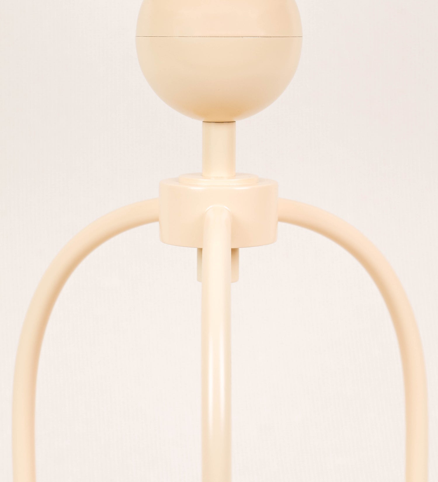 Candeeiro de mesa, de tom bege claro, com um design moderno e minimalista. O candeeiro tem o corpo com três pés curvados, terminando em pequenas esferas. A estrutura dos pés é interligada por uma peça central esférica. O cabo é revestido têxtil com um padrão de linhas douradas e brancas entrelaçadas, com interruptor e ficha transparentes.