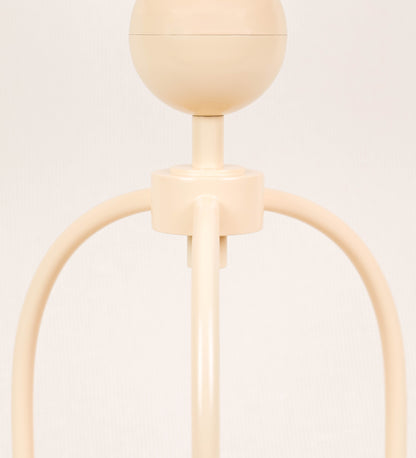 Candeeiro de mesa, de tom bege claro, com um design moderno e minimalista. O candeeiro tem o corpo com três pés curvados, terminando em pequenas esferas. A estrutura dos pés é interligada por uma peça central esférica. O cabo é revestido têxtil com um padrão de linhas douradas e brancas entrelaçadas, com interruptor e ficha transparentes.