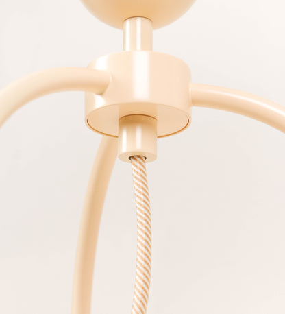 Candeeiro de mesa, de tom bege claro, com um design moderno e minimalista. O candeeiro tem o corpo com três pés curvados, terminando em pequenas esferas. A estrutura dos pés é interligada por uma peça central esférica. O cabo é revestido têxtil com um padrão de linhas douradas e brancas entrelaçadas, com interruptor e ficha transparentes.