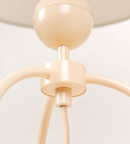Candeeiro de mesa, de tom bege claro, com um design moderno e minimalista. O candeeiro tem o corpo com três pés curvados, terminando em pequenas esferas. A estrutura dos pés é interligada por uma peça central esférica. O cabo é revestido têxtil com um padrão de linhas douradas e brancas entrelaçadas, com interruptor e ficha transparentes.