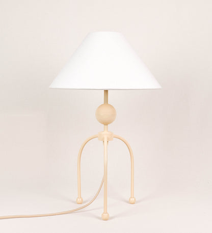 Candeeiro de mesa, de tom bege claro, com um design moderno e minimalista. O candeeiro tem o corpo com três pés curvados, terminando em pequenas esferas. A estrutura dos pés é interligada por uma peça central esférica. O cabo é revestido têxtil com um padrão de linhas douradas e brancas entrelaçadas, com interruptor e ficha transparentes. O abatjour é de forma cónica, em algodão, de tom bege claro com pequenas pintas escuras, semelhante à baunilha.