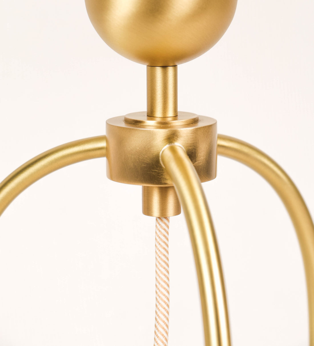 Candeeiro de mesa, em latão escovado, conferindo-lhe um tom dourado mate, com um design moderno e minimalista. O candeeiro tem o corpo com três pés curvados, terminando em pequenas esferas. A estrutura dos pés é interligada por uma peça central esférica. O cabo é revestido têxtil com um padrão de linhas douradas e brancas entrelaçadas, com interruptor e ficha transparentes. 