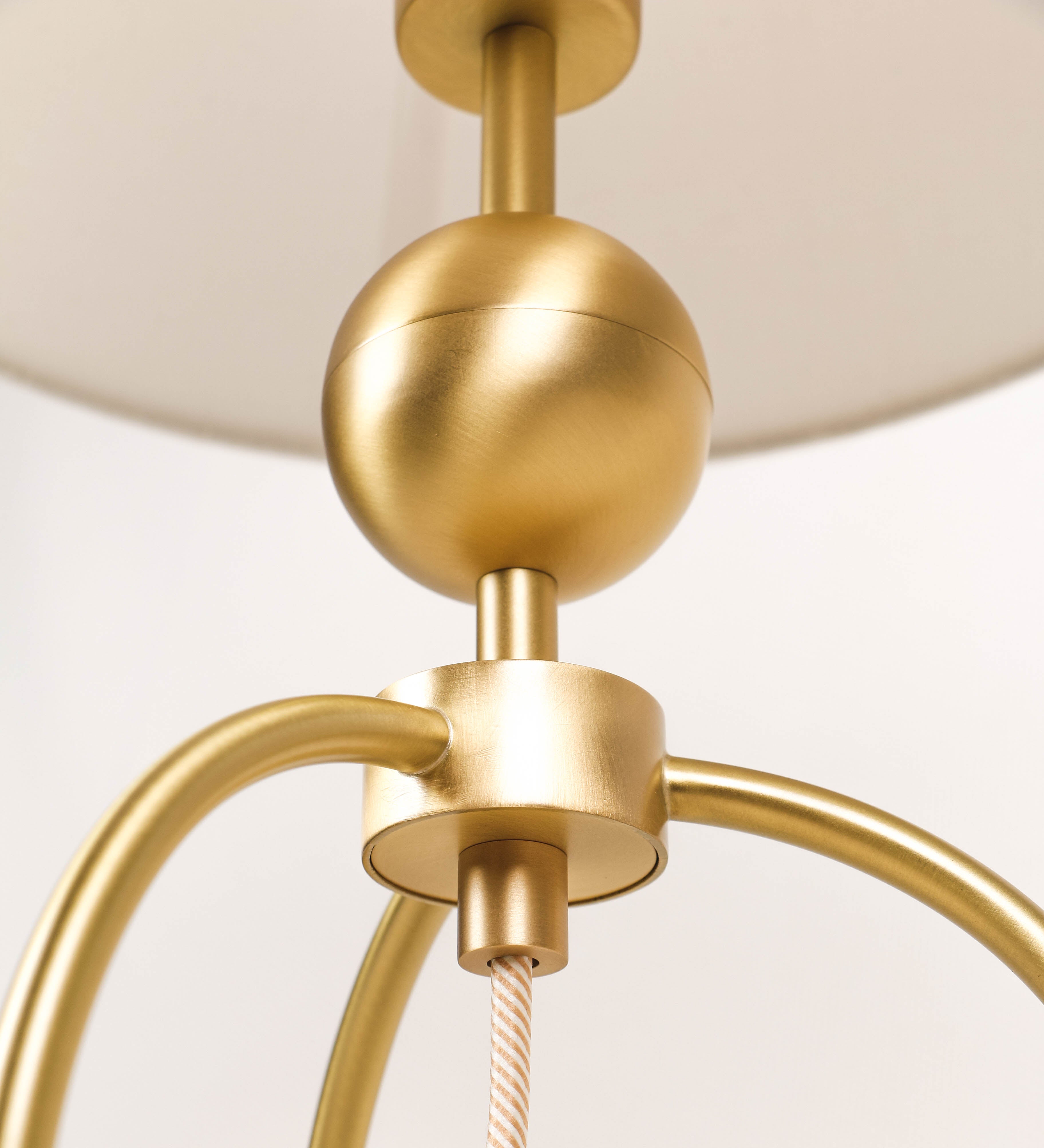 Candeeiro de mesa, em latão escovado, conferindo-lhe um tom dourado mate, com um design moderno e minimalista. O candeeiro tem o corpo com três pés curvados, terminando em pequenas esferas. A estrutura dos pés é interligada por uma peça central esférica. O cabo é revestido têxtil com um padrão de linhas douradas e brancas entrelaçadas, com interruptor e ficha transparentes. O abatjour é de forma cónica, em algodão, de tom bege claro com pequenas pintas escuras, semelhante à baunilha.
