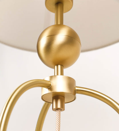 Candeeiro de mesa, em latão escovado, conferindo-lhe um tom dourado mate, com um design moderno e minimalista. O candeeiro tem o corpo com três pés curvados, terminando em pequenas esferas. A estrutura dos pés é interligada por uma peça central esférica. O cabo é revestido têxtil com um padrão de linhas douradas e brancas entrelaçadas, com interruptor e ficha transparentes. O abatjour é de forma cónica, em algodão, de tom bege claro com pequenas pintas escuras, semelhante à baunilha.