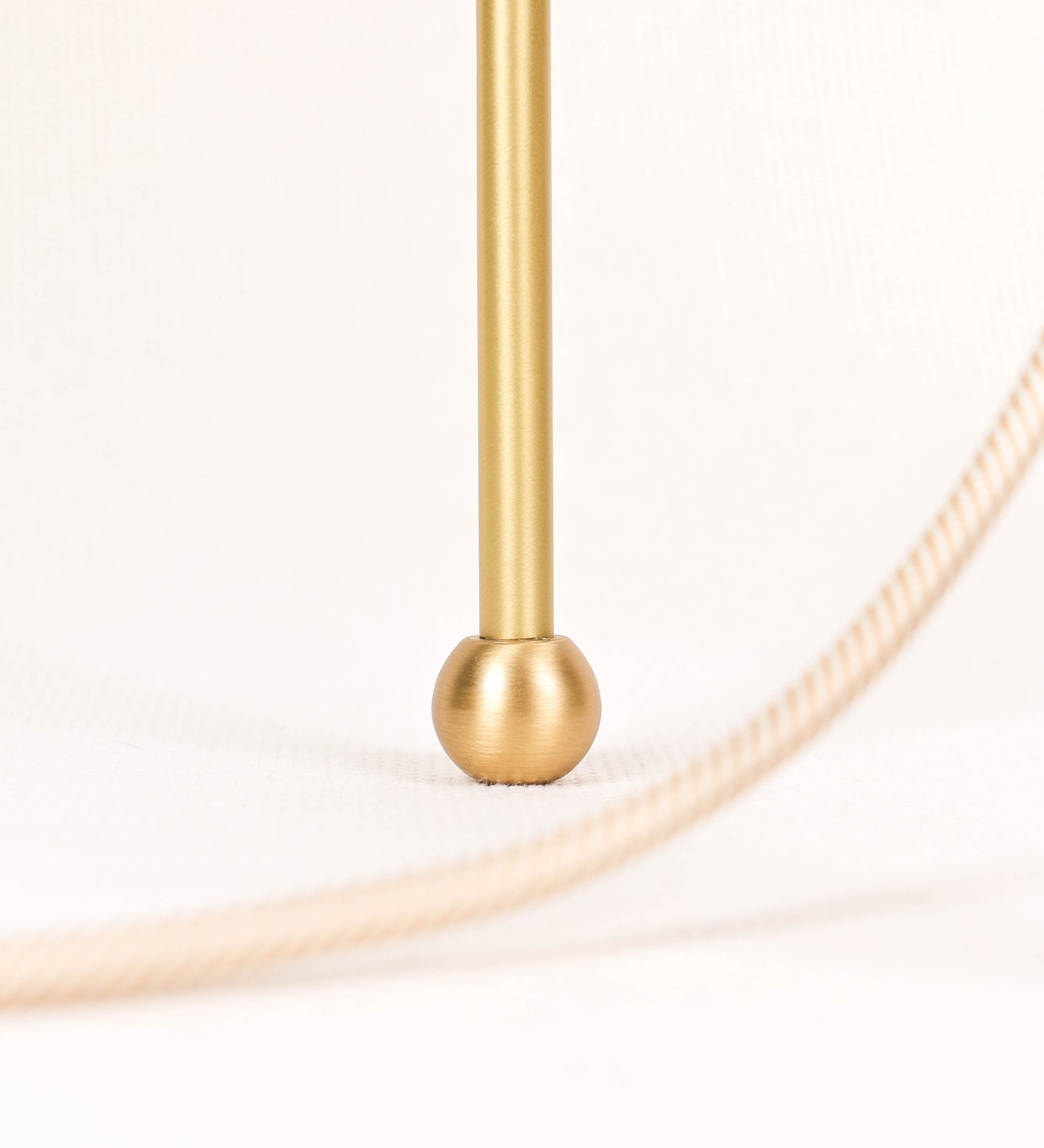 Candeeiro de mesa, em latão escovado, conferindo-lhe um tom dourado mate, com um design moderno e minimalista. O candeeiro tem o corpo com três pés curvados, terminando em pequenas esferas. A estrutura dos pés é interligada por uma peça central esférica. O cabo é revestido têxtil com um padrão de linhas douradas e brancas entrelaçadas, com interruptor e ficha transparentes. 