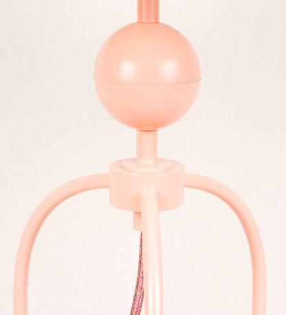 Candeeiro de mesa, de tom rosa salmão, com um design moderno e minimalista. O candeeiro tem o corpo com três pés curvados, terminando em pequenas esferas. A estrutura dos pés é interligada por uma peça central esférica. O cabo é revestido têxtil de tom rosa velho, com interruptor e ficha transparentes. O abatjour é de forma cónica, em algodão, de tom bege claro com pequenas pintas escuras, semelhante à baunilha.