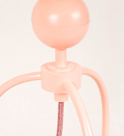 Candeeiro de mesa, de tom rosa salmão, com um design moderno e minimalista. O candeeiro tem o corpo com três pés curvados, terminando em pequenas esferas. A estrutura dos pés é interligada por uma peça central esférica. O cabo é revestido têxtil de tom rosa velho, com interruptor e ficha transparentes. O abatjour é de forma cónica, em algodão, de tom bege claro com pequenas pintas escuras, semelhante à baunilha.