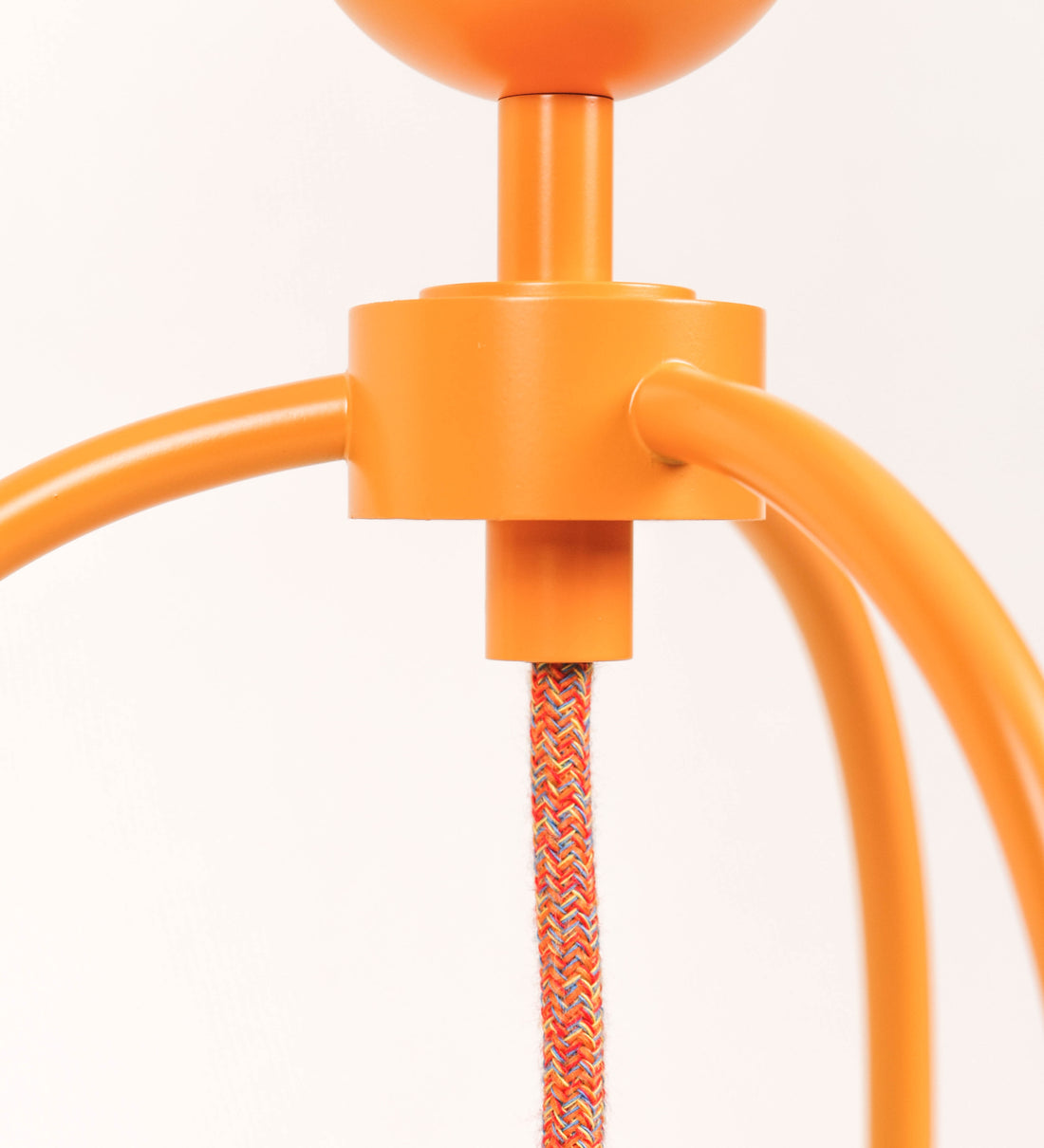 Candeeiro de mesa, de tom laranja-tangerina, com um design moderno e minimalista. O candeeiro tem o corpo com três pés curvados, terminando em pequenas esferas. A estrutura dos pés é interligada por uma peça central esférica. O cabo é revestido têxtil com um padrão de linhas coloridas (laranjas, azuis, amarelas e outras), com interruptor e ficha transparentes.