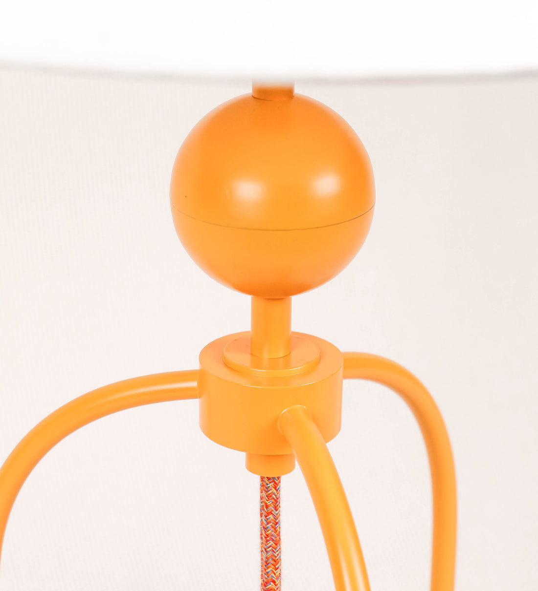 Candeeiro de mesa, de tom laranja-tangerina, com um design moderno e minimalista. O candeeiro tem o corpo com três pés curvados, terminando em pequenas esferas. A estrutura dos pés é interligada por uma peça central esférica. O cabo é revestido têxtil com um padrão de linhas coloridas, com interruptor e ficha transparentes. O abatjour é de forma cónica, em algodão, de tom bege claro com pequenas pintas escuras, semelhante à baunilha.