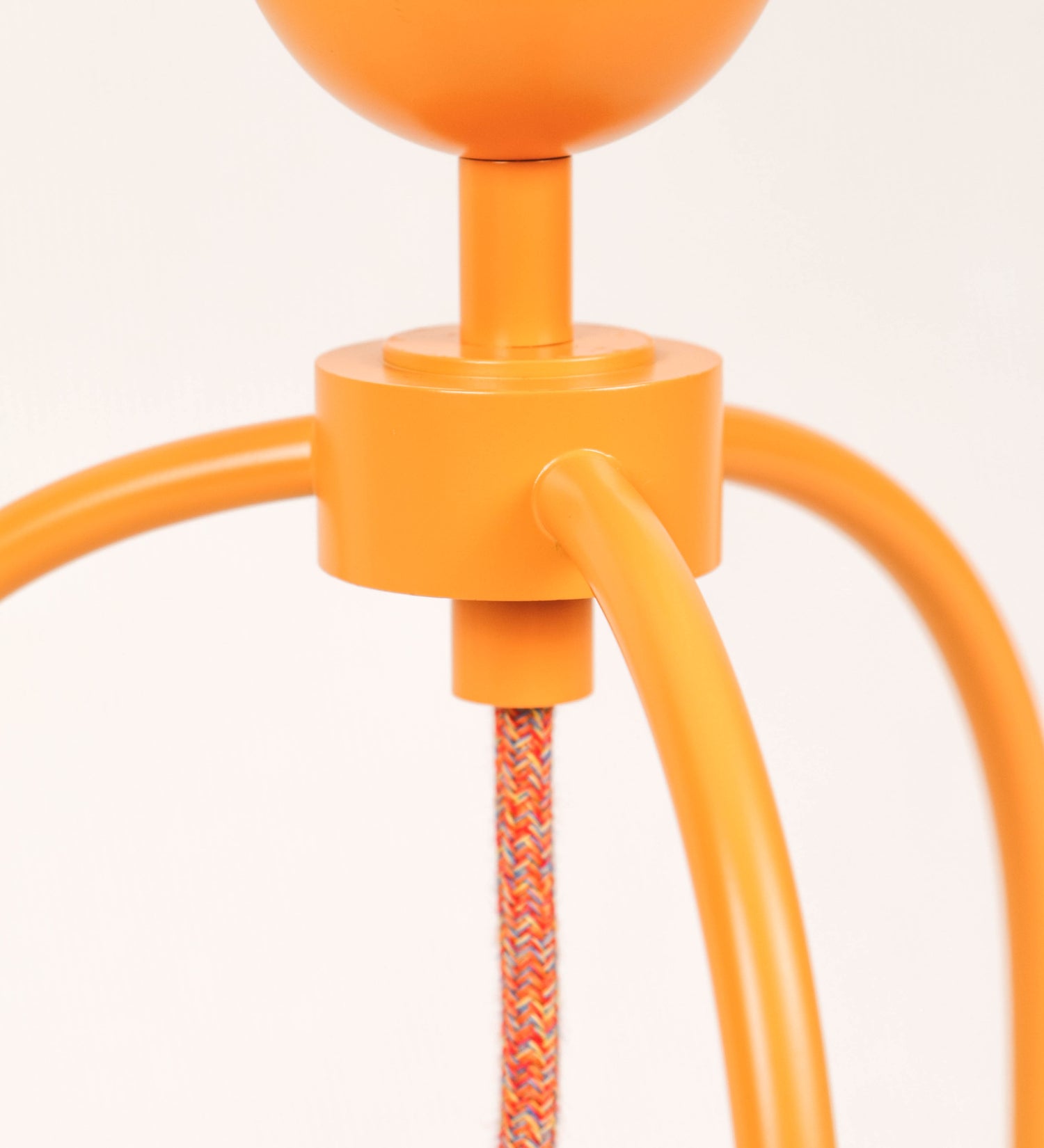 Candeeiro de mesa, de tom laranja-tangerina, com um design moderno e minimalista. O candeeiro tem o corpo com três pés curvados, terminando em pequenas esferas. A estrutura dos pés é interligada por uma peça central esférica. O cabo é revestido têxtil com um padrão de linhas coloridas, com interruptor e ficha transparentes. O abatjour é de forma cónica, em algodão, de tom bege claro com pequenas pintas escuras, semelhante à baunilha.