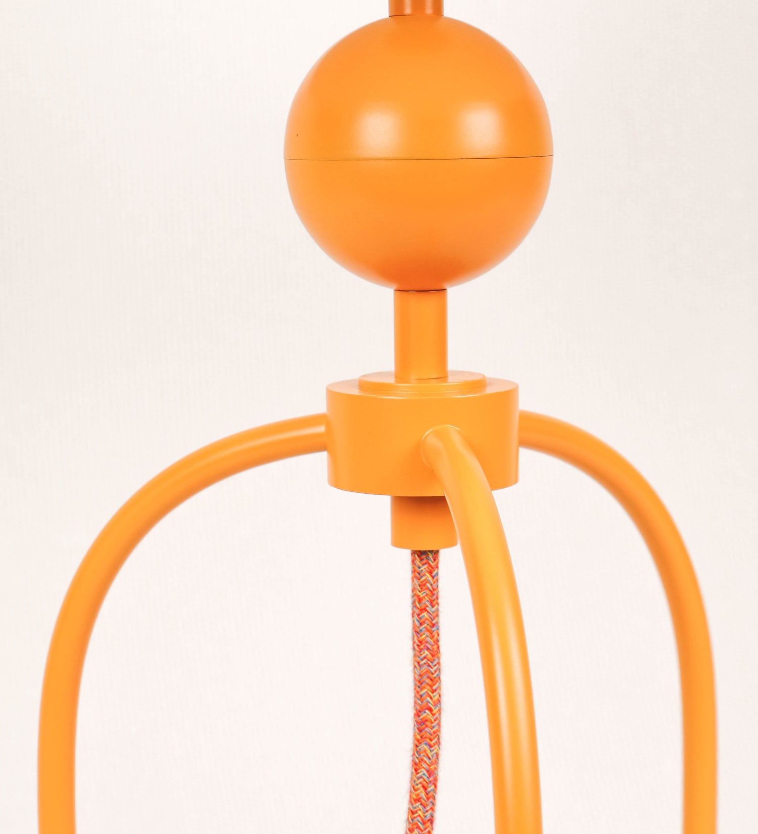 Candeeiro de mesa, de tom laranja-tangerina, com um design moderno e minimalista. O candeeiro tem o corpo com três pés curvados, terminando em pequenas esferas. A estrutura dos pés é interligada por uma peça central esférica. O cabo é revestido têxtil com um padrão de linhas coloridas, com interruptor e ficha transparentes. O abatjour é de forma cónica, em algodão, de tom bege claro com pequenas pintas escuras, semelhante à baunilha.