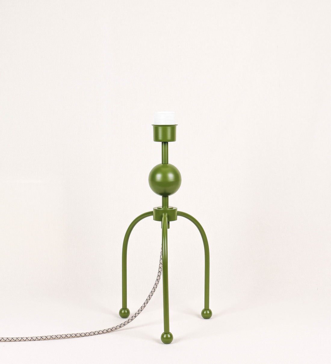 Candeeiro de mesa, de tom verde couve-de-bruxelas, com um design moderno e minimalista. O candeeiro tem o corpo com três pés curvados, terminando em pequenas esferas. A estrutura dos pés é interligada por uma peça central esférica. O cabo é revestido têxtil com um padrão de linhas castanhas e beges entrelaçadas, com interruptor e ficha transparentes.