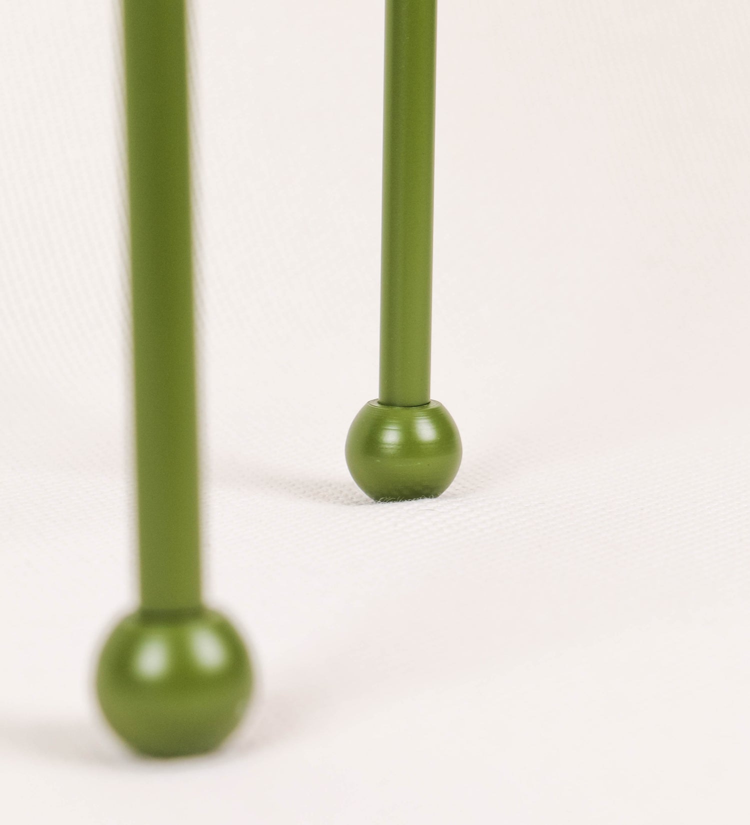 Candeeiro de mesa, de tom verde couve-de-bruxelas, com um design moderno e minimalista. O candeeiro tem o corpo com três pés curvados, terminando em pequenas esferas. A estrutura dos pés é interligada por uma peça central esférica. O cabo é revestido têxtil com um padrão de linhas castanhas e beges entrelaçadas, com interruptor e ficha transparentes. O abatjour é de forma cónica, em algodão, de tom bege claro com pequenas pintas escuras, semelhante à baunilha.