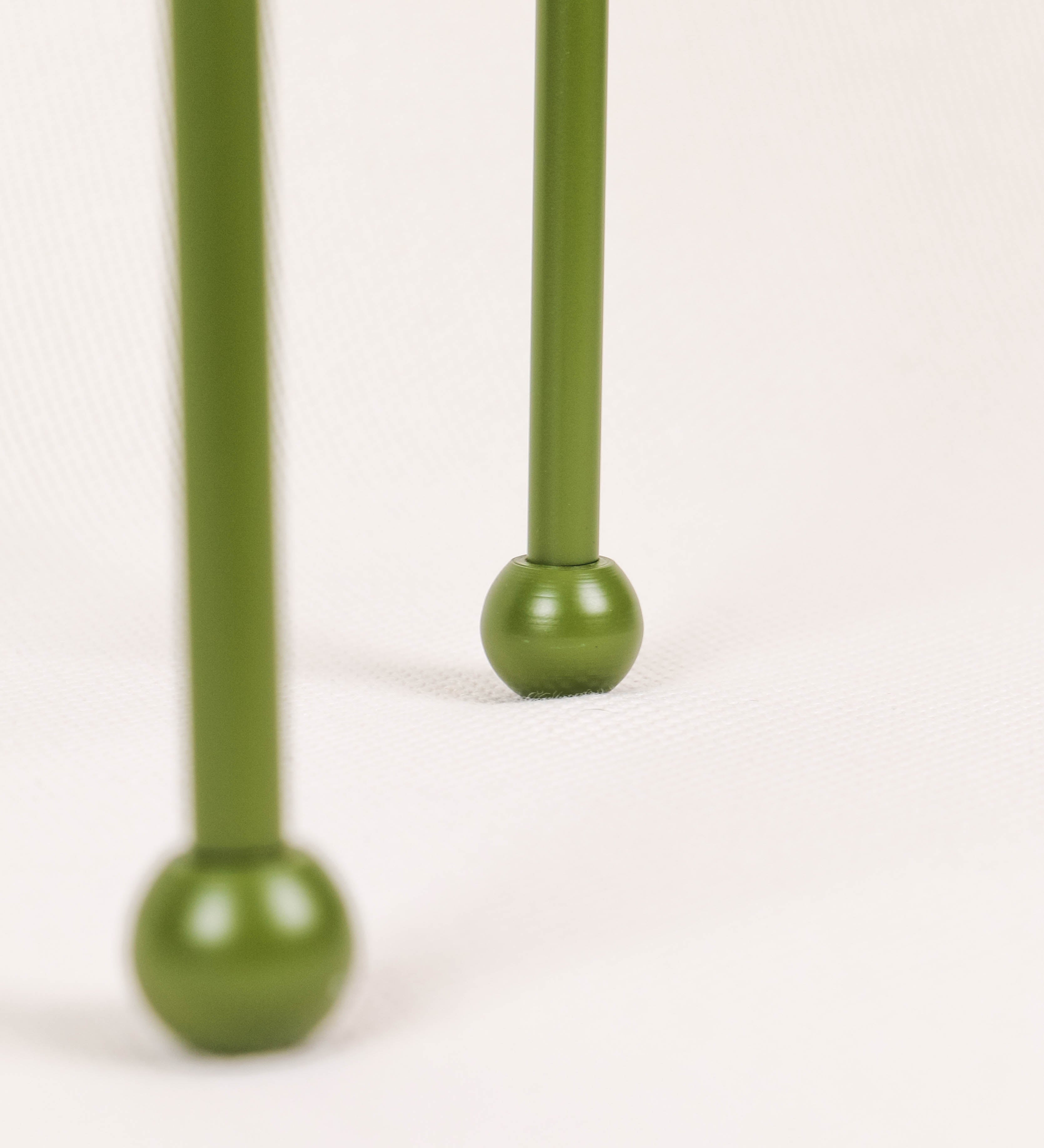 Candeeiro de mesa, de tom verde couve-de-bruxelas, com um design moderno e minimalista. O candeeiro tem o corpo com três pés curvados, terminando em pequenas esferas. A estrutura dos pés é interligada por uma peça central esférica. O cabo é revestido têxtil com um padrão de linhas castanhas e beges entrelaçadas, com interruptor e ficha transparentes. O abatjour é de forma cónica, em algodão, de tom bege claro com pequenas pintas escuras, semelhante à baunilha.