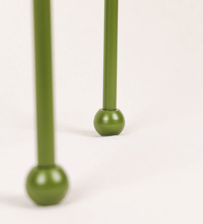 Candeeiro de mesa, de tom verde couve-de-bruxelas, com um design moderno e minimalista. O candeeiro tem o corpo com três pés curvados, terminando em pequenas esferas. A estrutura dos pés é interligada por uma peça central esférica. O cabo é revestido têxtil com um padrão de linhas castanhas e beges entrelaçadas, com interruptor e ficha transparentes. O abatjour é de forma cónica, em algodão, de tom bege claro com pequenas pintas escuras, semelhante à baunilha.