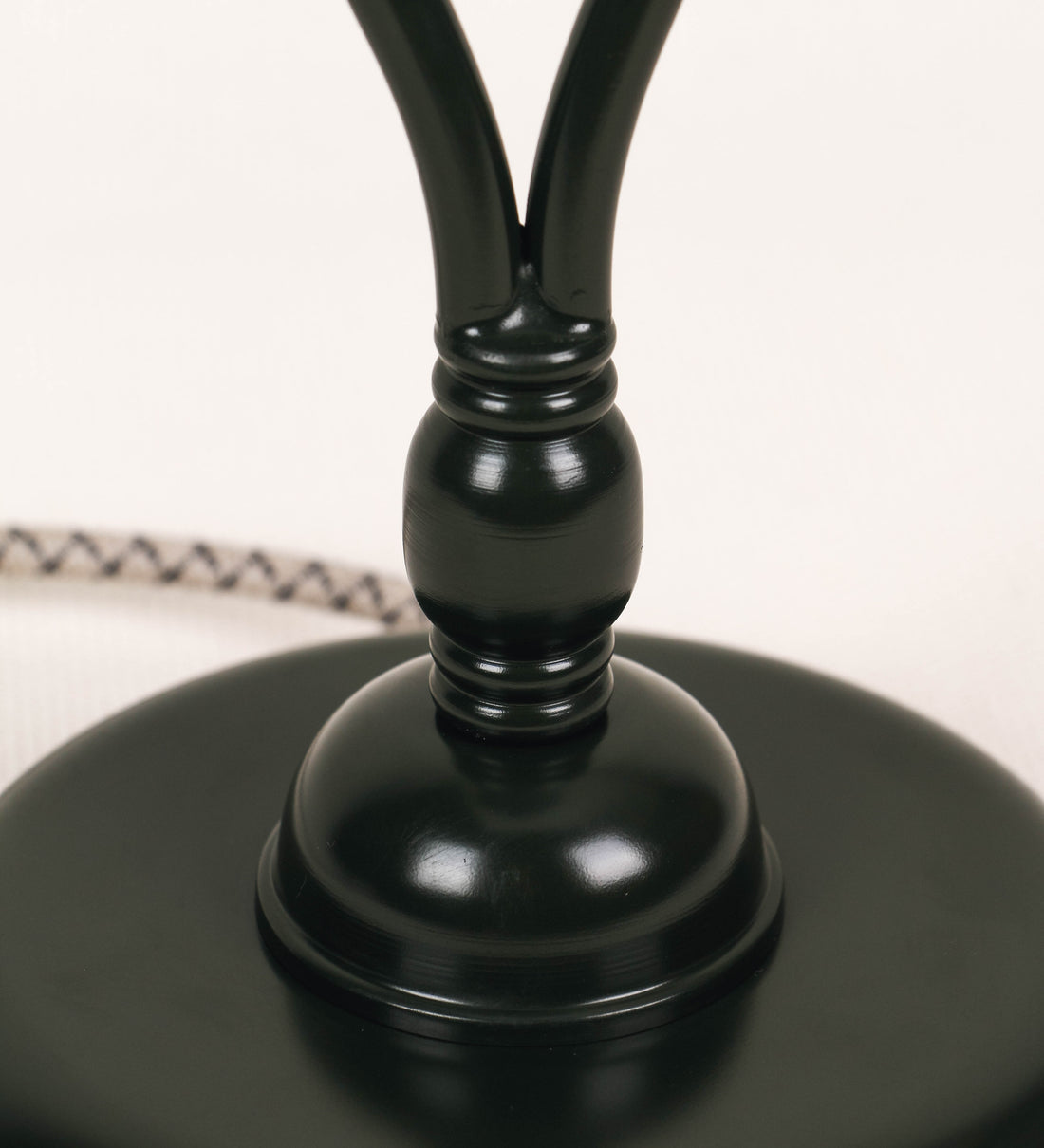 Candeeiro de mesa com um design clássico e sofisticado. O candeeiro possui uma base circular e robusta de tom verde-azeitona. A estrutura da base é complementada por um suporte em forma de nó, também de tom verde-azeitona, que se eleva graciosamente até ao suporte da luz. A luz é difundida através de uma esfera de vidro fosco branco, assente no corpo. O cabo é revestido têxtil com um padrão trançado com linhas castanhas e beges, com interruptor e ficha transparentes.