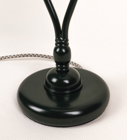 Candeeiro de mesa com um design clássico e sofisticado. O candeeiro possui uma base circular e robusta de tom verde-azeitona. A estrutura da base é complementada por um suporte em forma de nó, também de tom verde-azeitona, que se eleva graciosamente até ao suporte da luz. A luz é difundida através de uma esfera de vidro fosco branco, assente no corpo. O cabo é revestido têxtil com um padrão trançado com linhas castanhas e beges, com interruptor e ficha transparentes.
