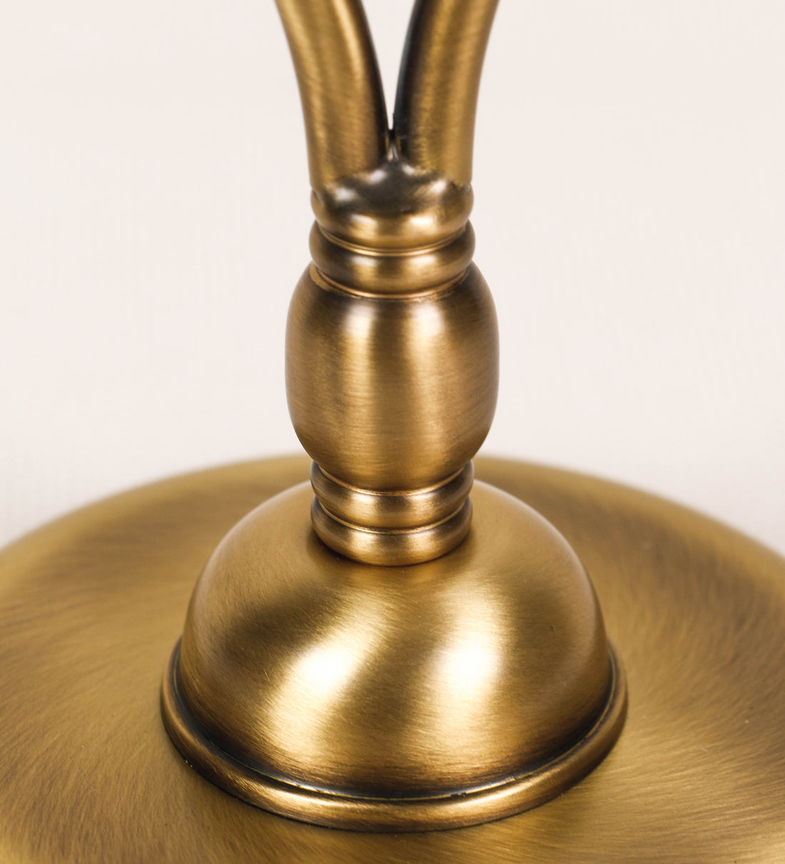 Candeeiro de mesa com um design clássico e sofisticado. O candeeiro possui uma base circular e robusta em latão com acabamento em ouro velho. A estrutura da base é complementada por um suporte em forma de nó, também em ouro velho, que se eleva graciosamente até ao suporte da luz. A luz é difundida através de uma esfera de vidro fosco branco, assente no corpo. O cabo é revestido têxtil com um padrão trançado de linhas douradas e brancas, com interruptor e ficha transparentes.