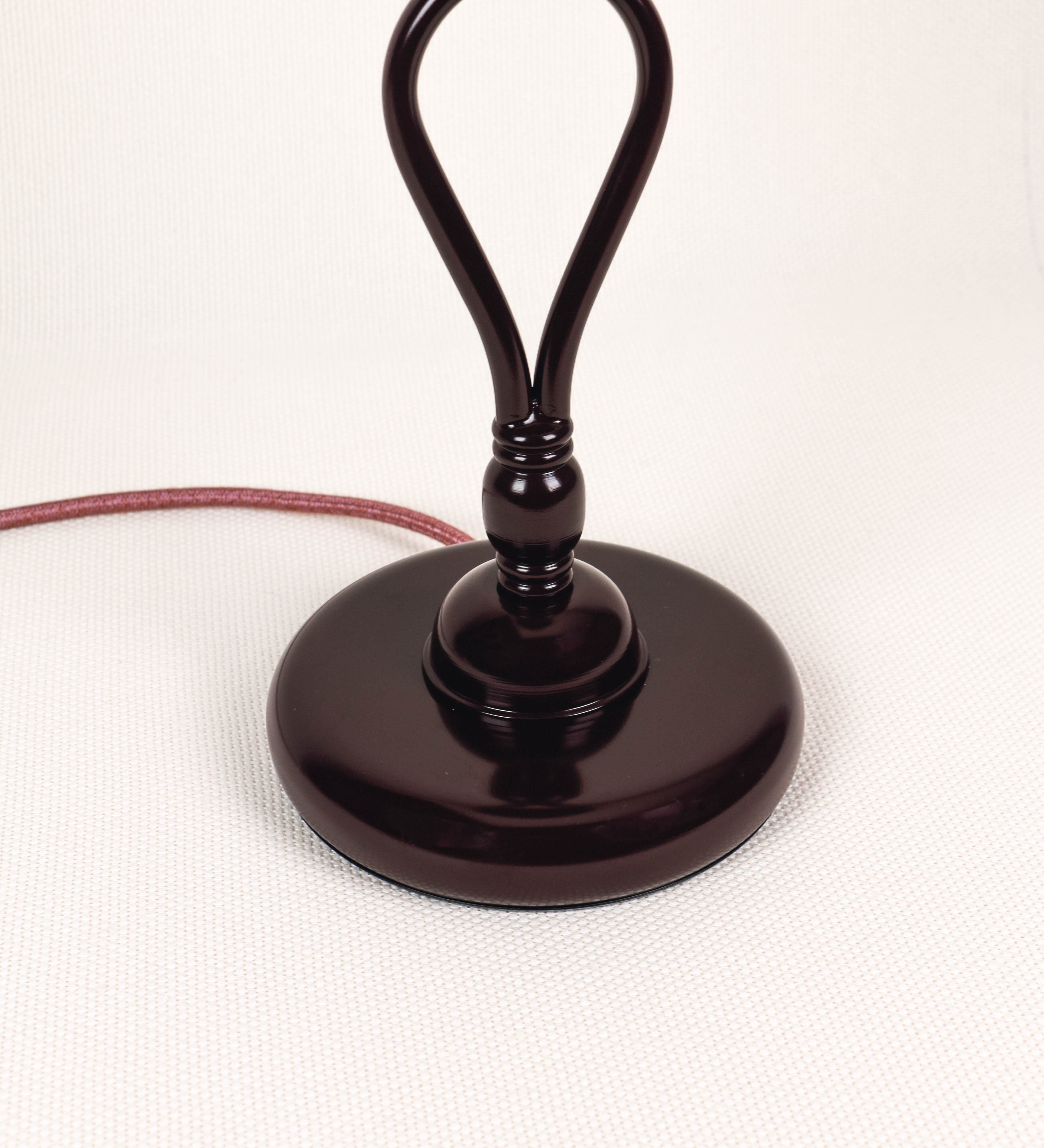 Candeeiro de mesa com um design clássico e sofisticado. O candeeiro possui uma base circular e robusta de tom vinho. A estrutura da base é complementada por um suporte em forma de nó, também de tom vinho, que se eleva graciosamente até ao suporte da luz. A luz é difundida através de uma esfera de vidro fosco branco, assente no corpo. O cabo é revestido têxtil de tom rosa velho, com interruptor e ficha transparentes.
