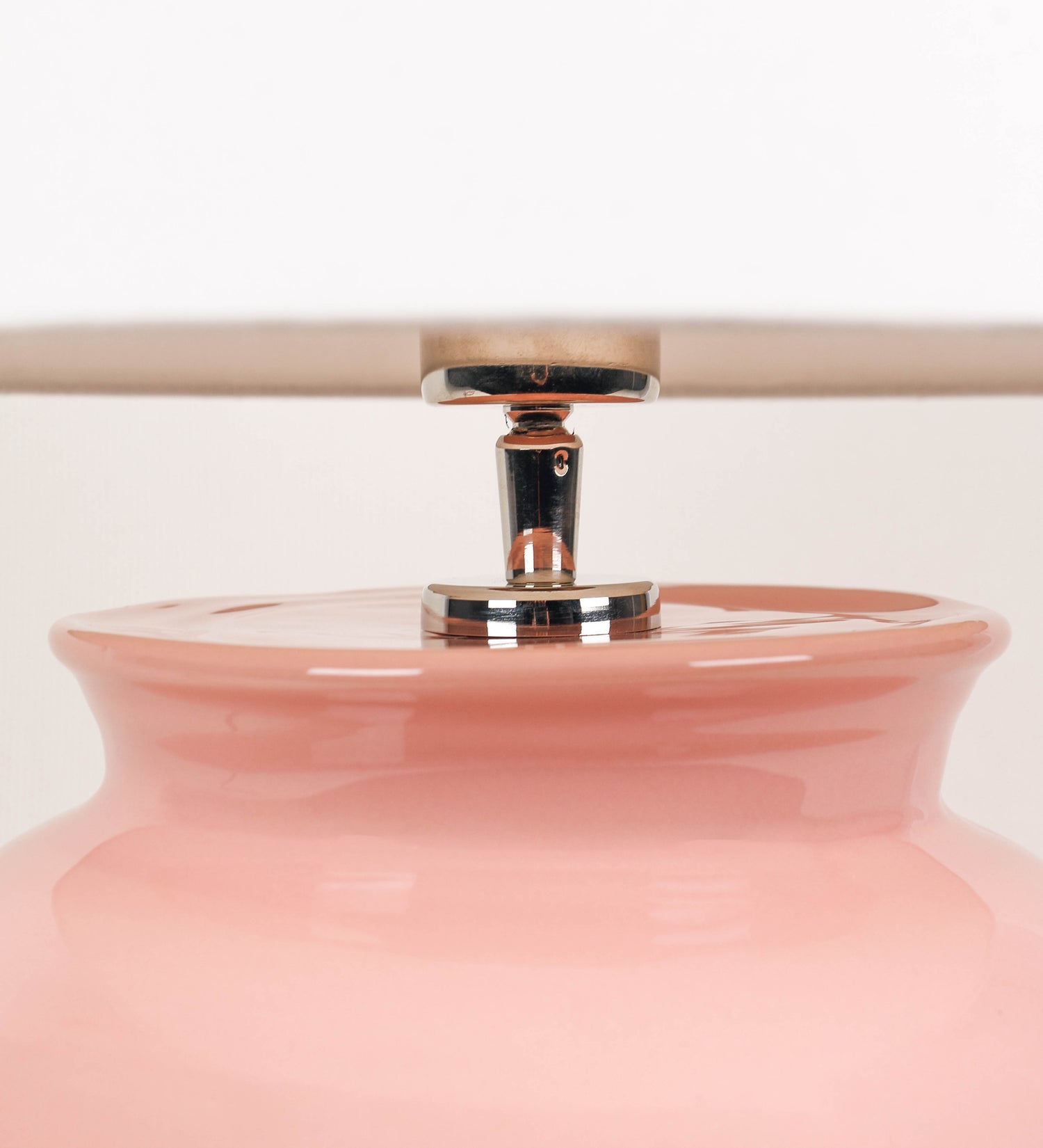 Candeeiro de mesa com um design rústico e sofisticado. A base do candeeiro é de barro vidrado de tom rosa salmão. A forma da base é arredondada com uma borda superior mais estreita, lembrando um vaso tradicional. A superfície da base é decorada com um padrão de relevos ovais. O suporte da lâmpada é em níquel polido e é manipulável. O cabo é revestido têxtil com um padrão trançado de tom rosa velho, com interruptor e ficha transparentes. O abatjour é cónico, em algodão, de tom bege claro.
